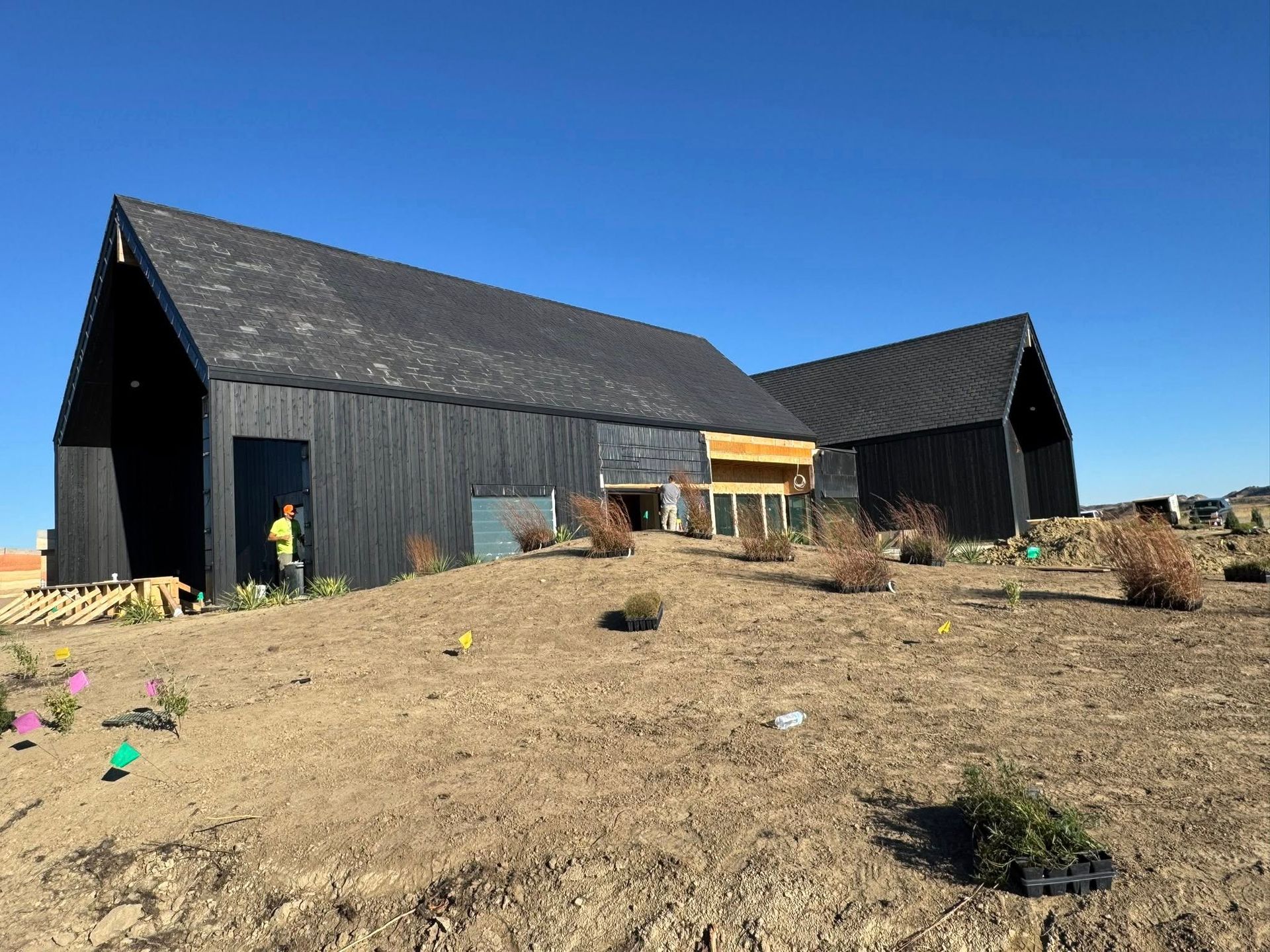 Black modern buildings on a dry hillside under a clear blue sky with a person near the left building