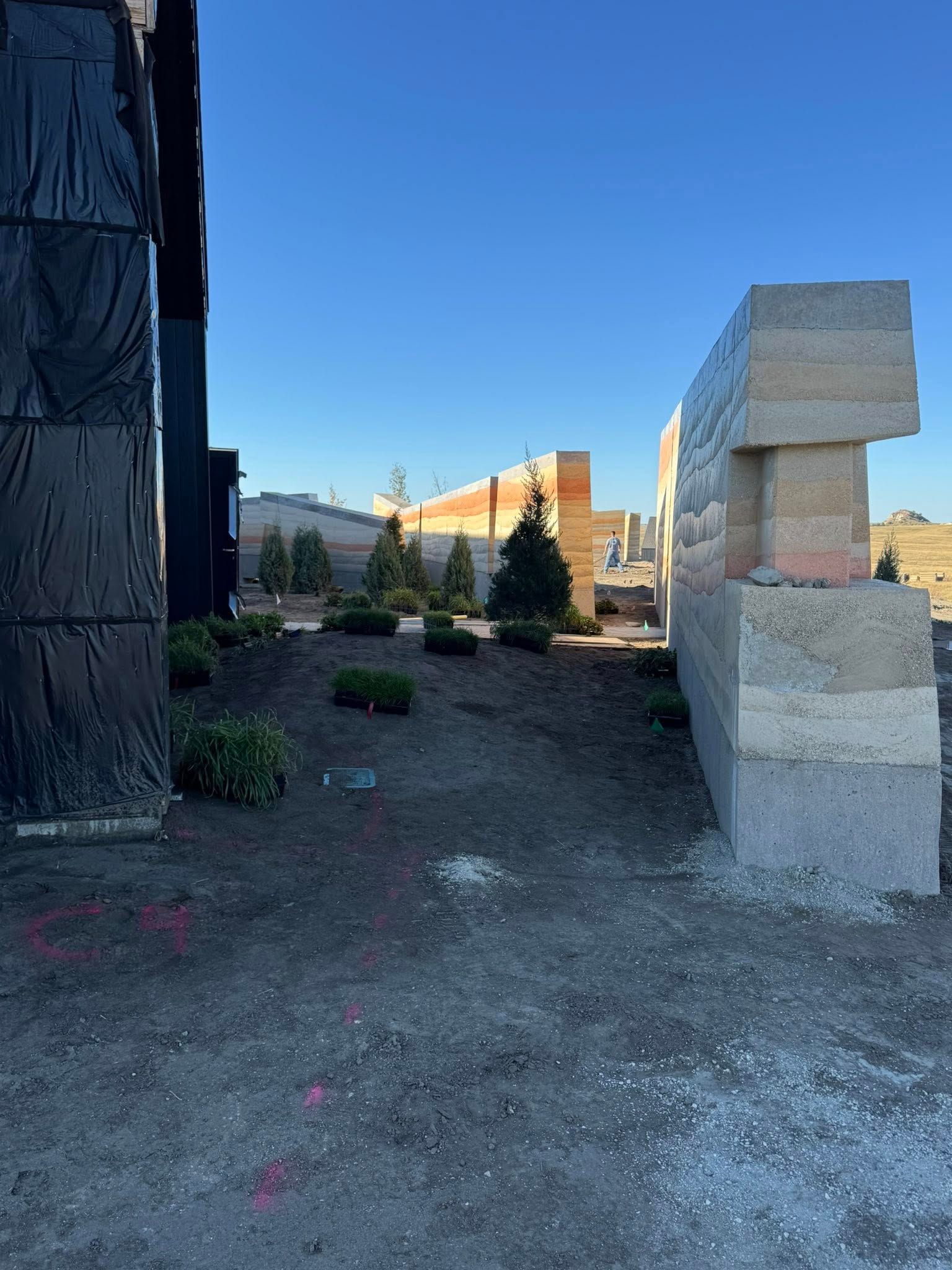 Outdoor gravel path beside a stone building, with mountains and blue sky in the distance.