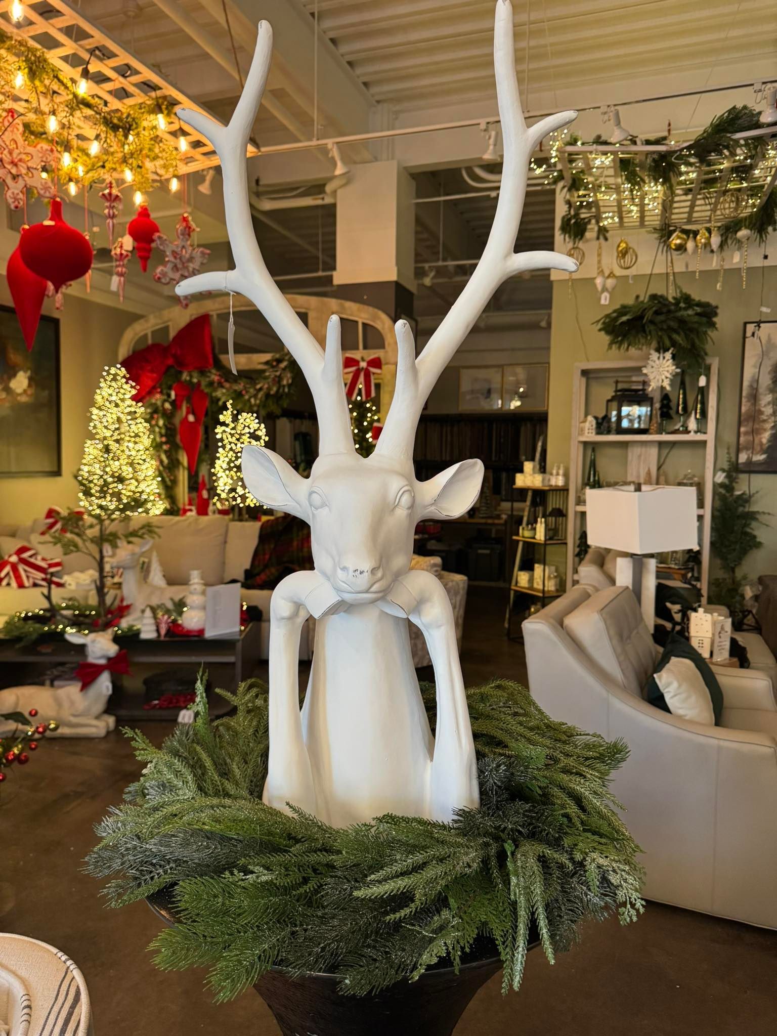 White deer sculpture in a festive shop display with holiday decorations and greenery
