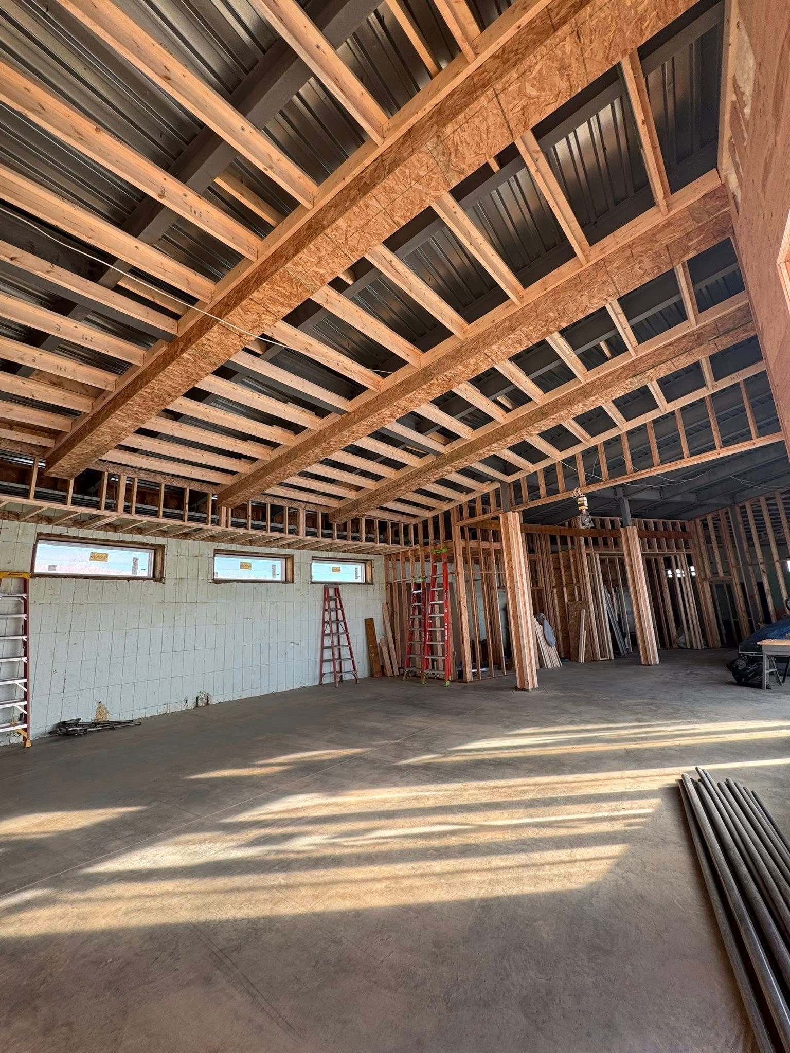 Interior of a construction site with exposed wooden ceiling beams, drywall, and scattered building materials