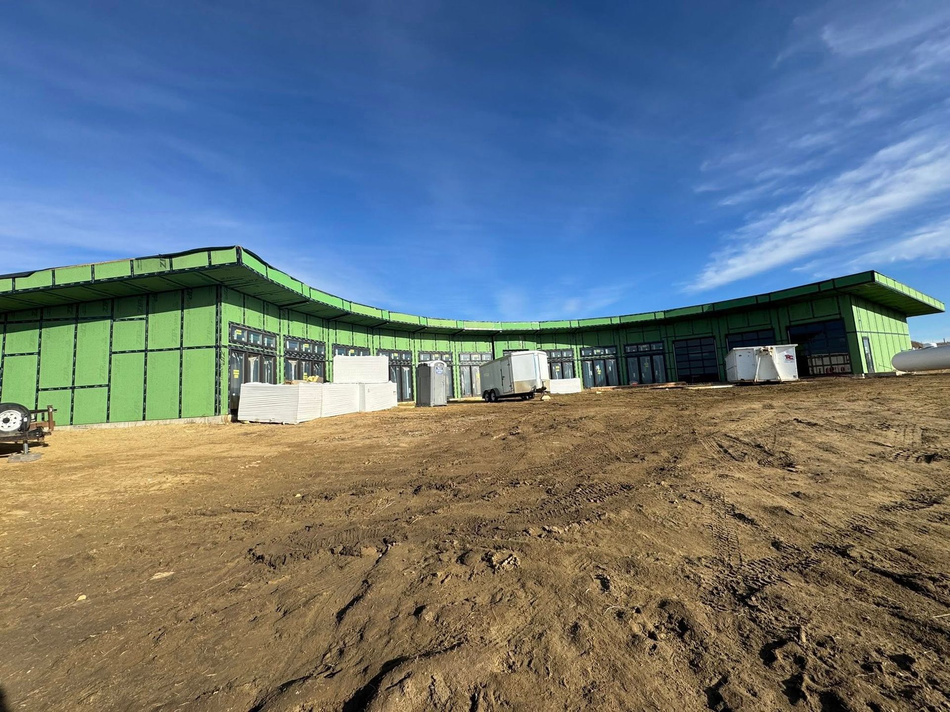 Green industrial building with a curved roof on a dirt lot under a clear blue sky