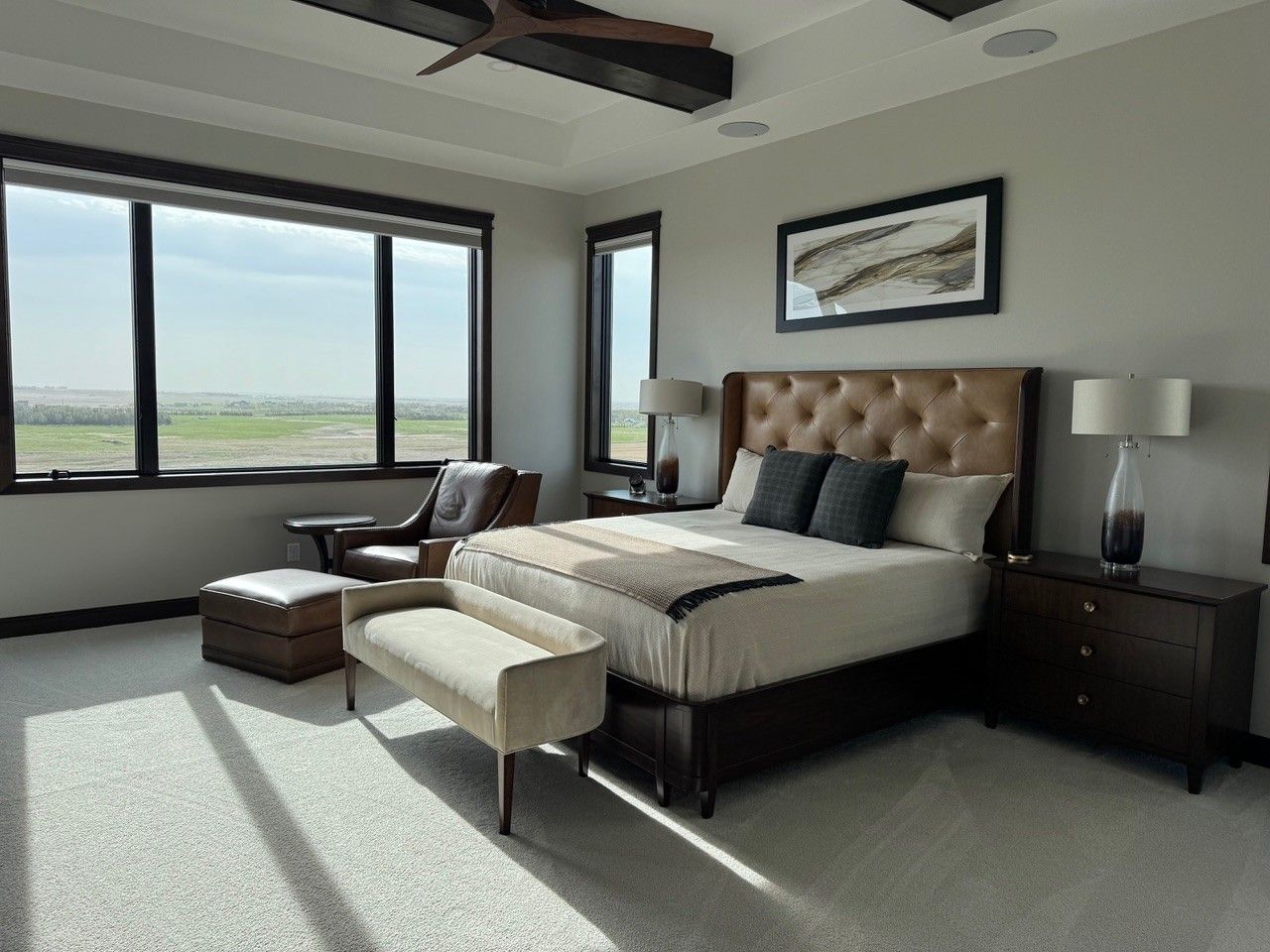 Modern bedroom with a tufted bed, dark wood nightstands, and large windows overlooking a scenic view
