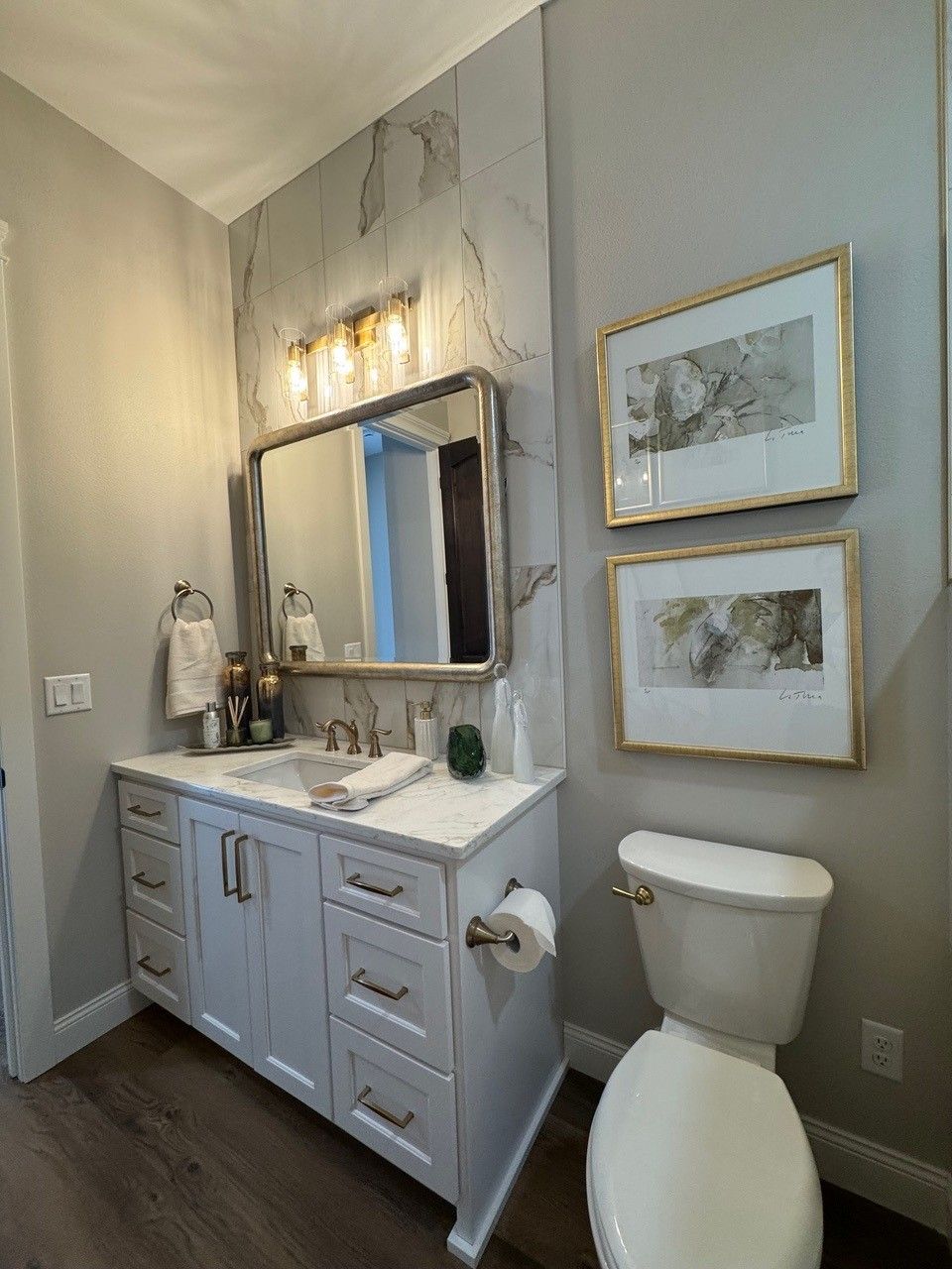 Bathroom with gray vanity, round mirror lights, framed art, and a toilet on the right.