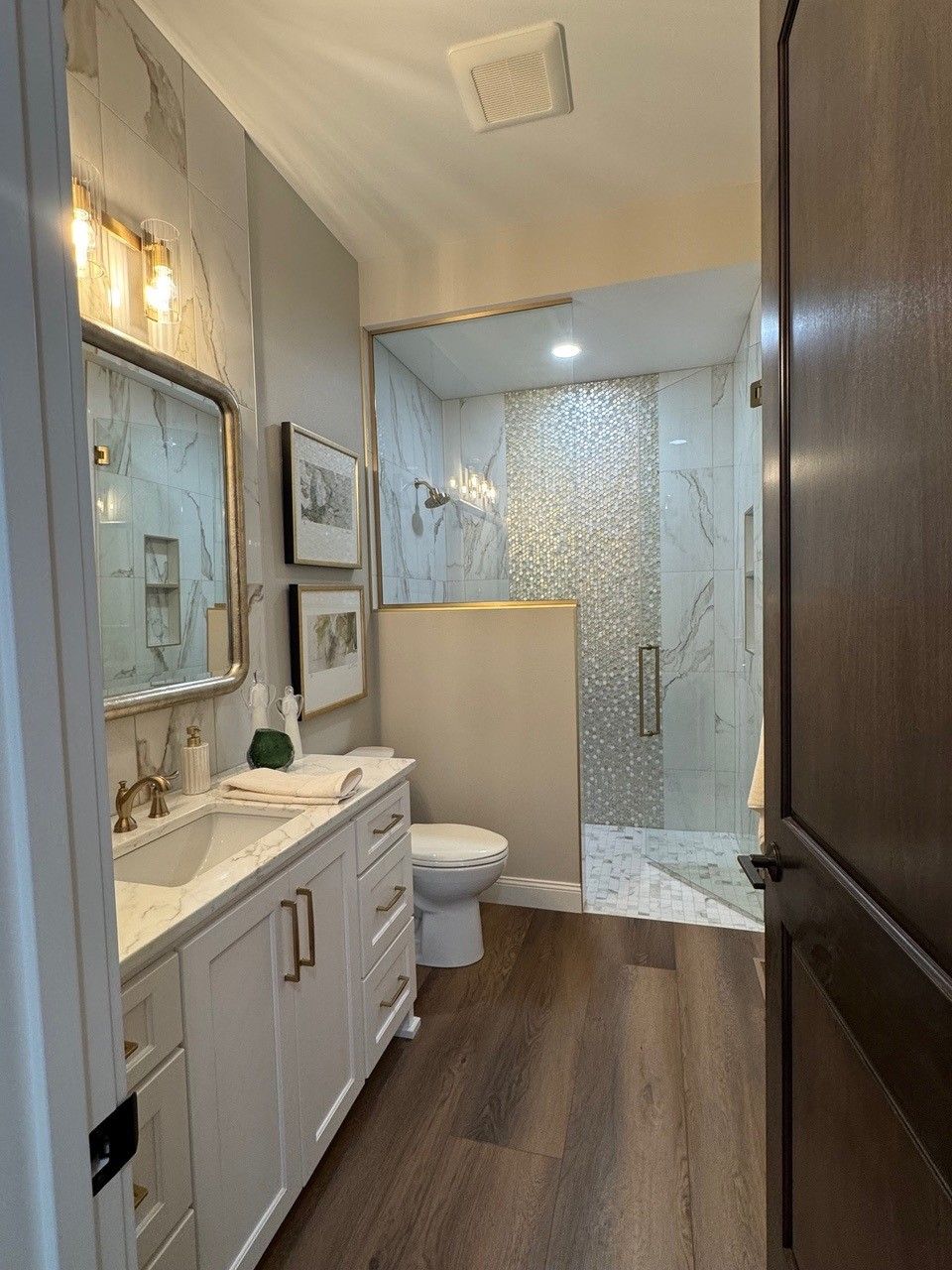 Bright bathroom with white vanity, toilet, wood floor, and glass shower enclosure