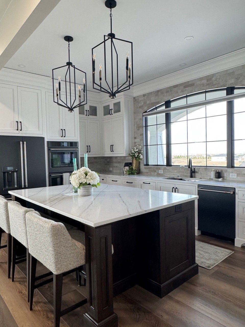 Modern kitchen with a large island, black cabinets, marble countertop, and geometric pendant lights