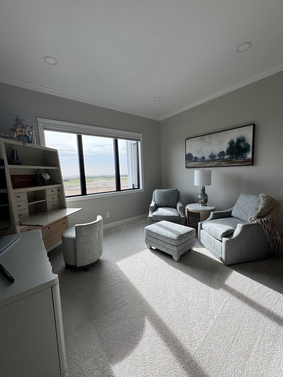 Bright living room with gray chairs, white ottoman, large window, and wall-mounted TV.