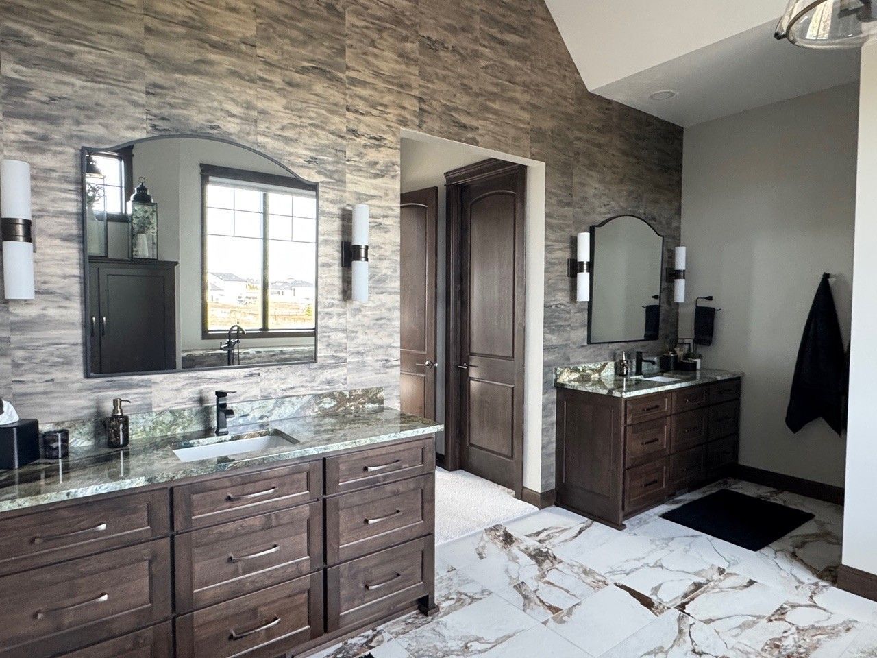 Modern bathroom with dark wood vanities, stone accent wall, and marble tile floor