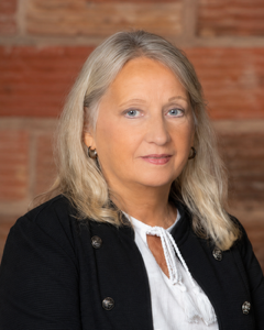 Portrait of a woman with gray hair in a black jacket against a brick wall background