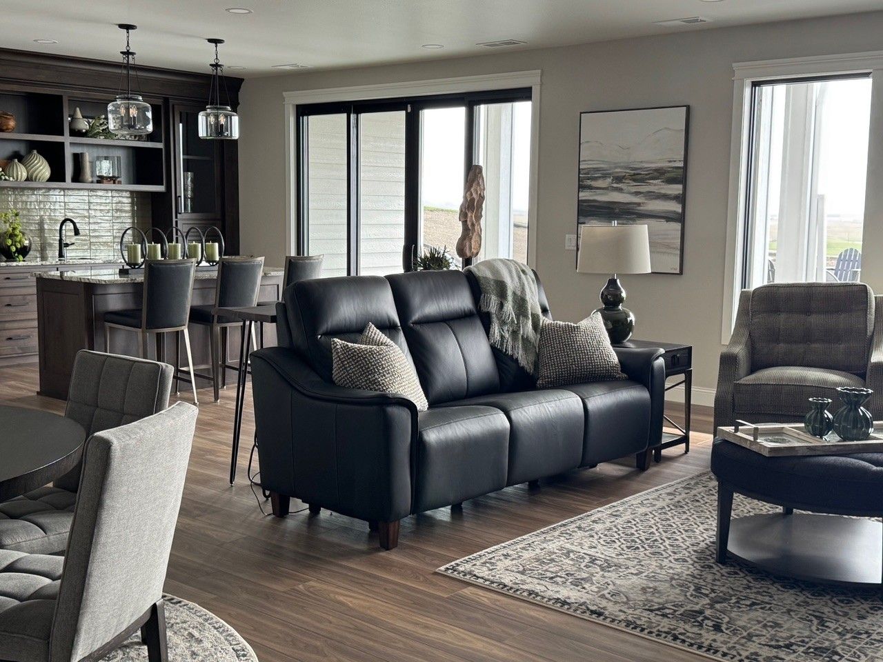 Modern living room with black leather sofa, armchairs, coffee table, and large windows