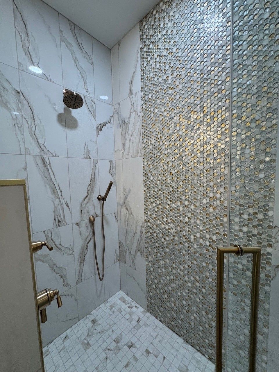 Modern tiled shower with marble walls, mosaic accent wall, and brass fixtures