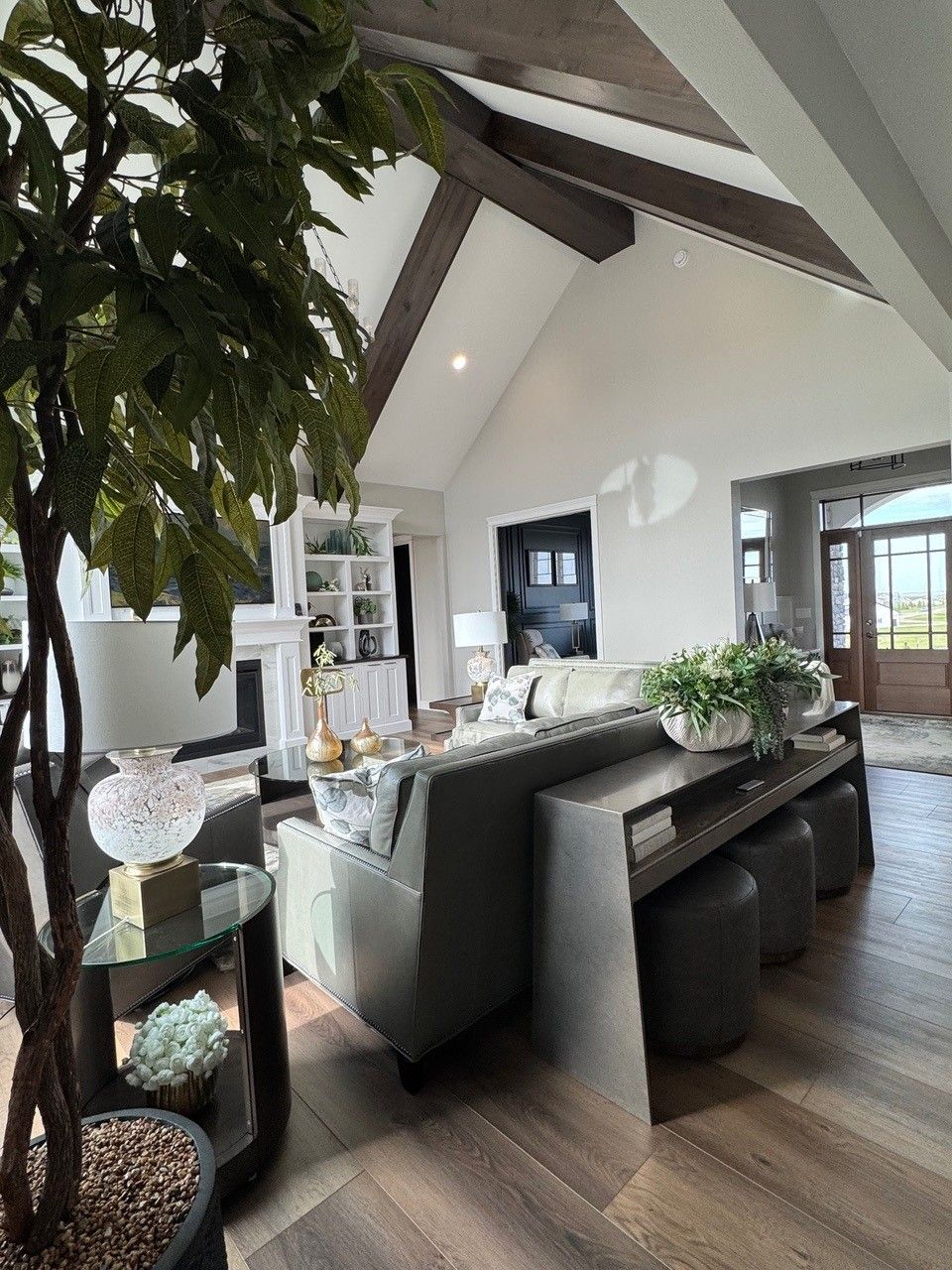 Modern living room with high vaulted ceiling, gray sectional sofa, dark wood floors, and large windows