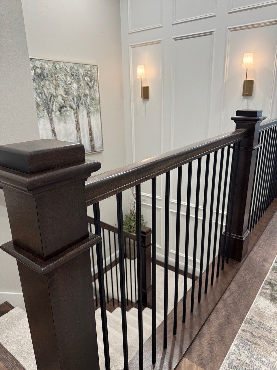 Elegant staircase with black railing, white walls, wall sconces, and abstract artwork.