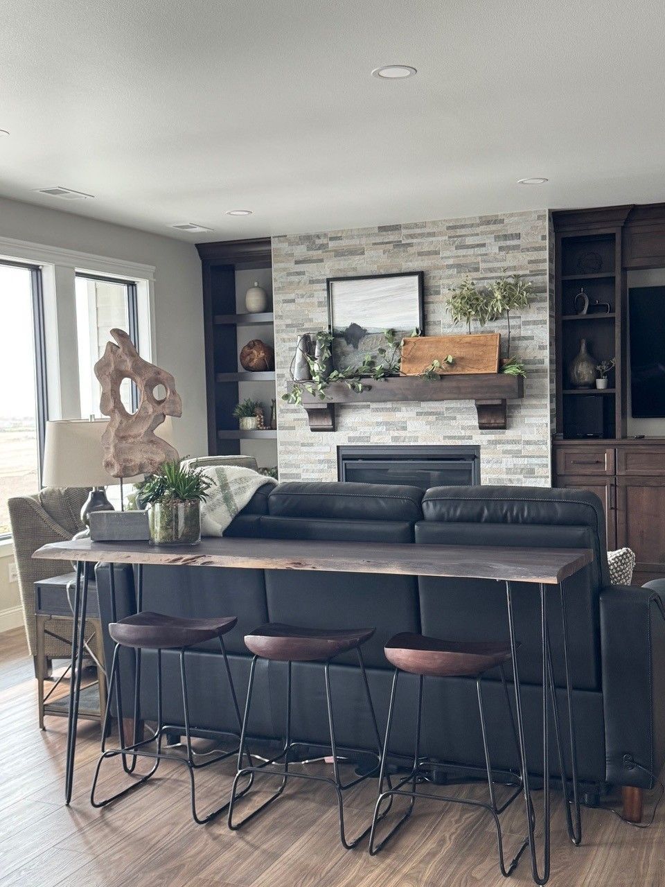 Bright living room with black sectional, fireplace, wall-mounted TV, and tall windows