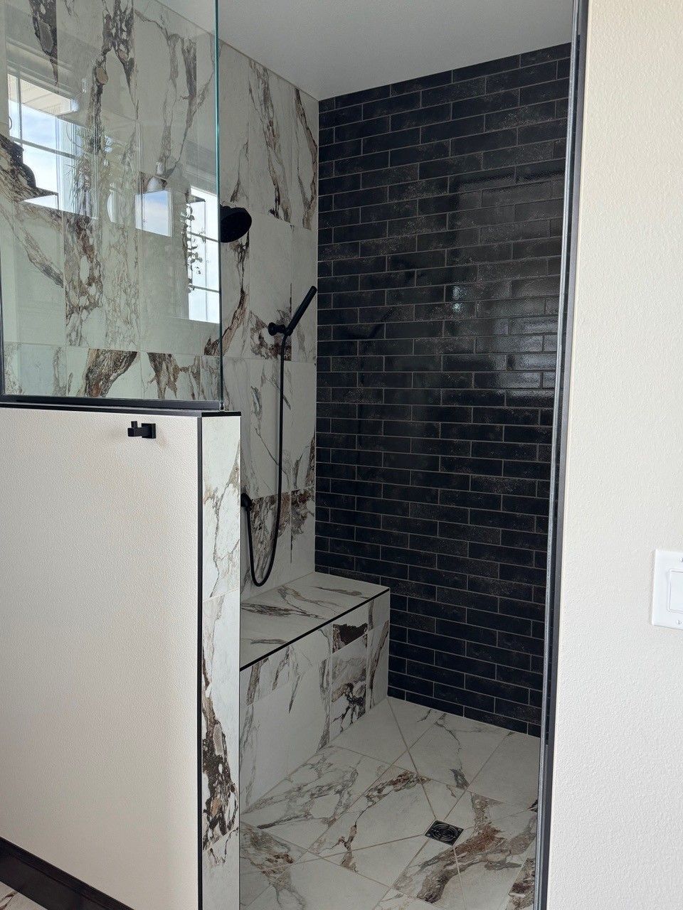 Marble-tiled shower nook with a black brick accent wall and white cabinet in the foreground