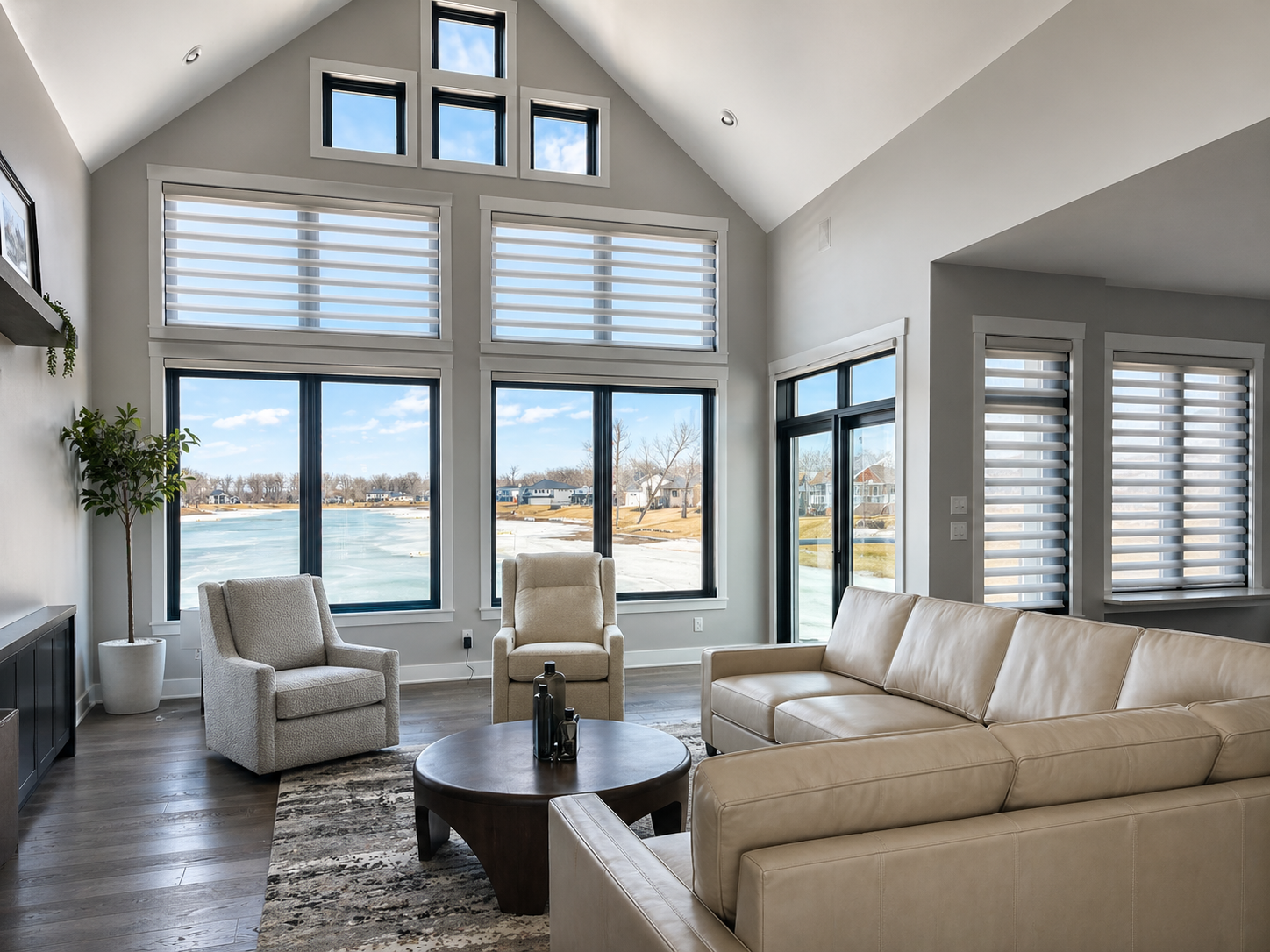 Bright modern living room with white sofas, armchairs, and large windows overlooking water.