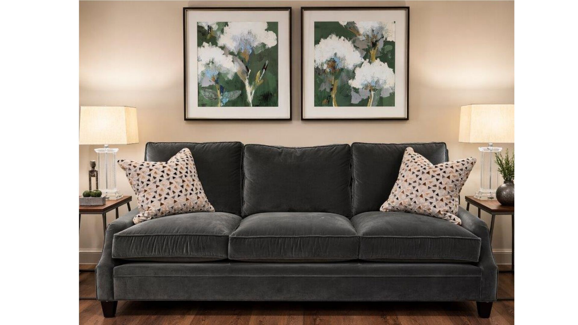 Dark gray sofa with patterned pillows between two lamps, under framed floral prints in a cozy living room.