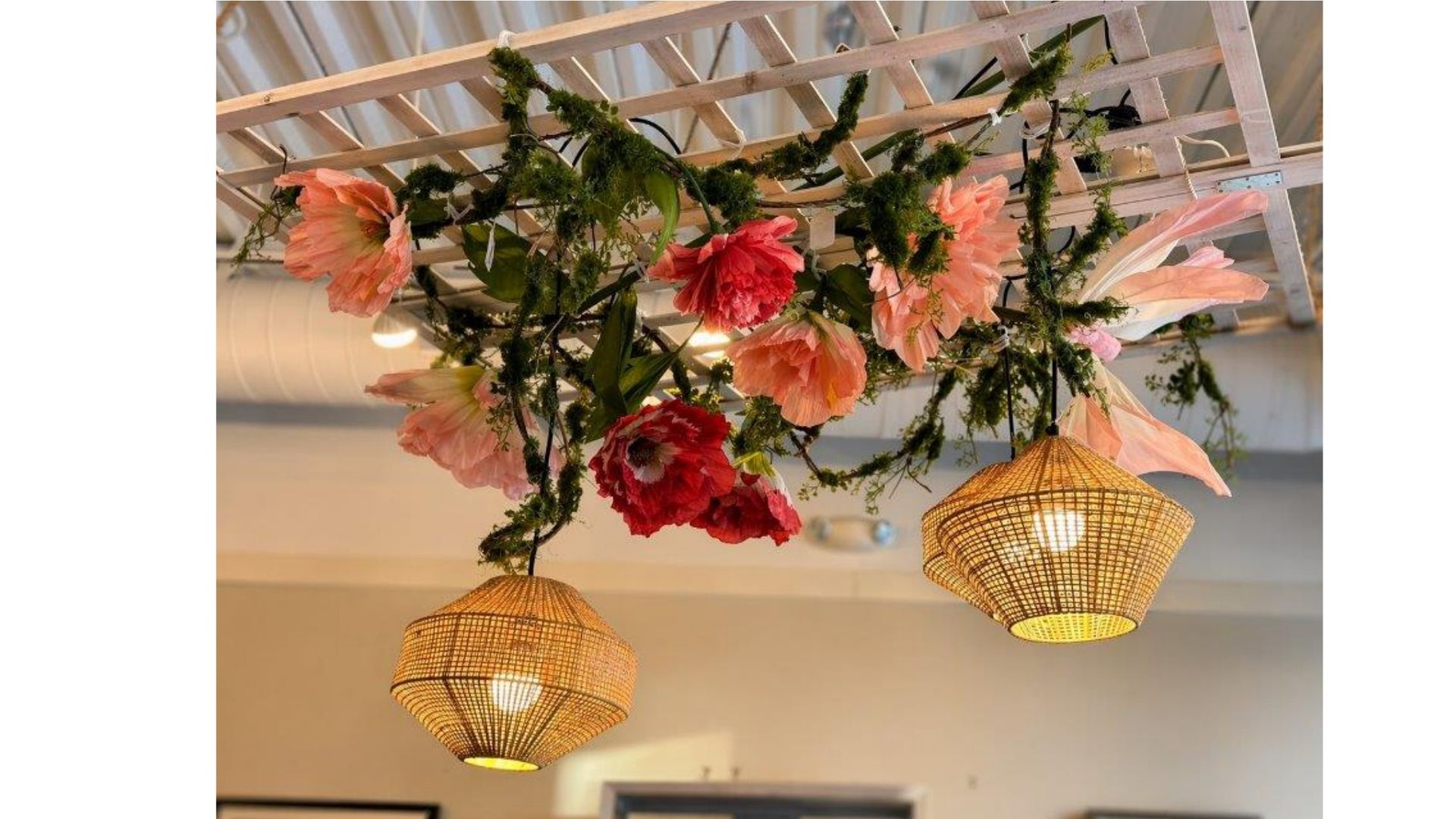 Decorative floral arrangement with pink flowers and hanging woven lanterns on a ceiling frame