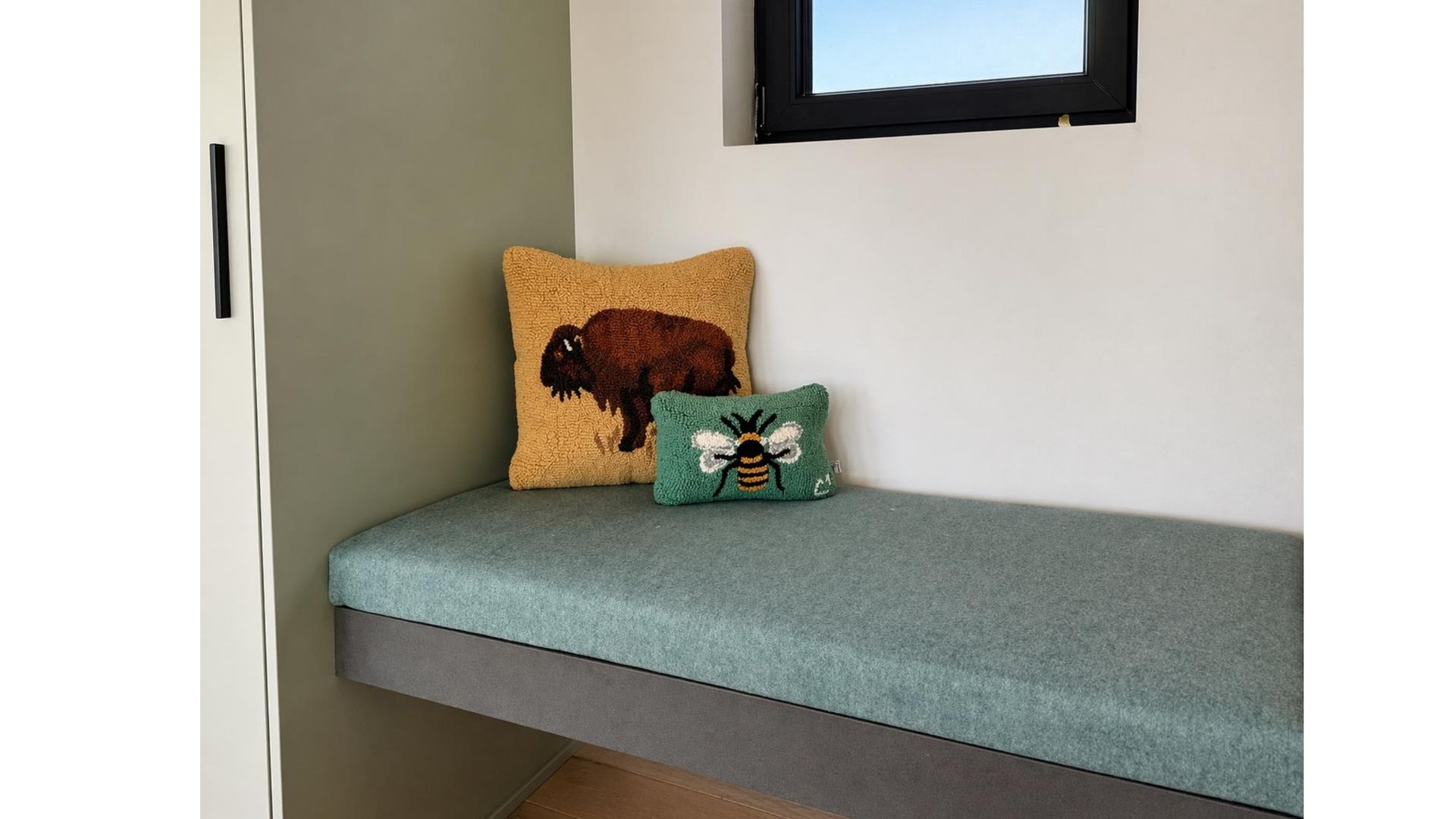 Small bench with teal cushion and two decorative pillows beside a window in a corner nook