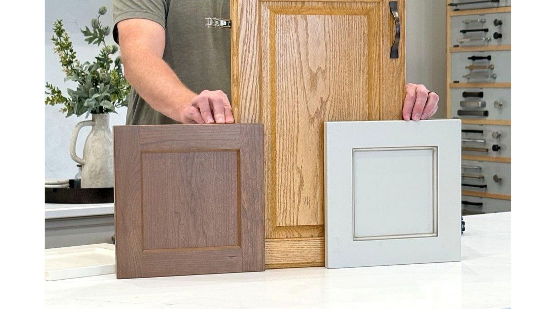 Hands holding three cabinet door samples in brown, wood grain, and white on a countertop.