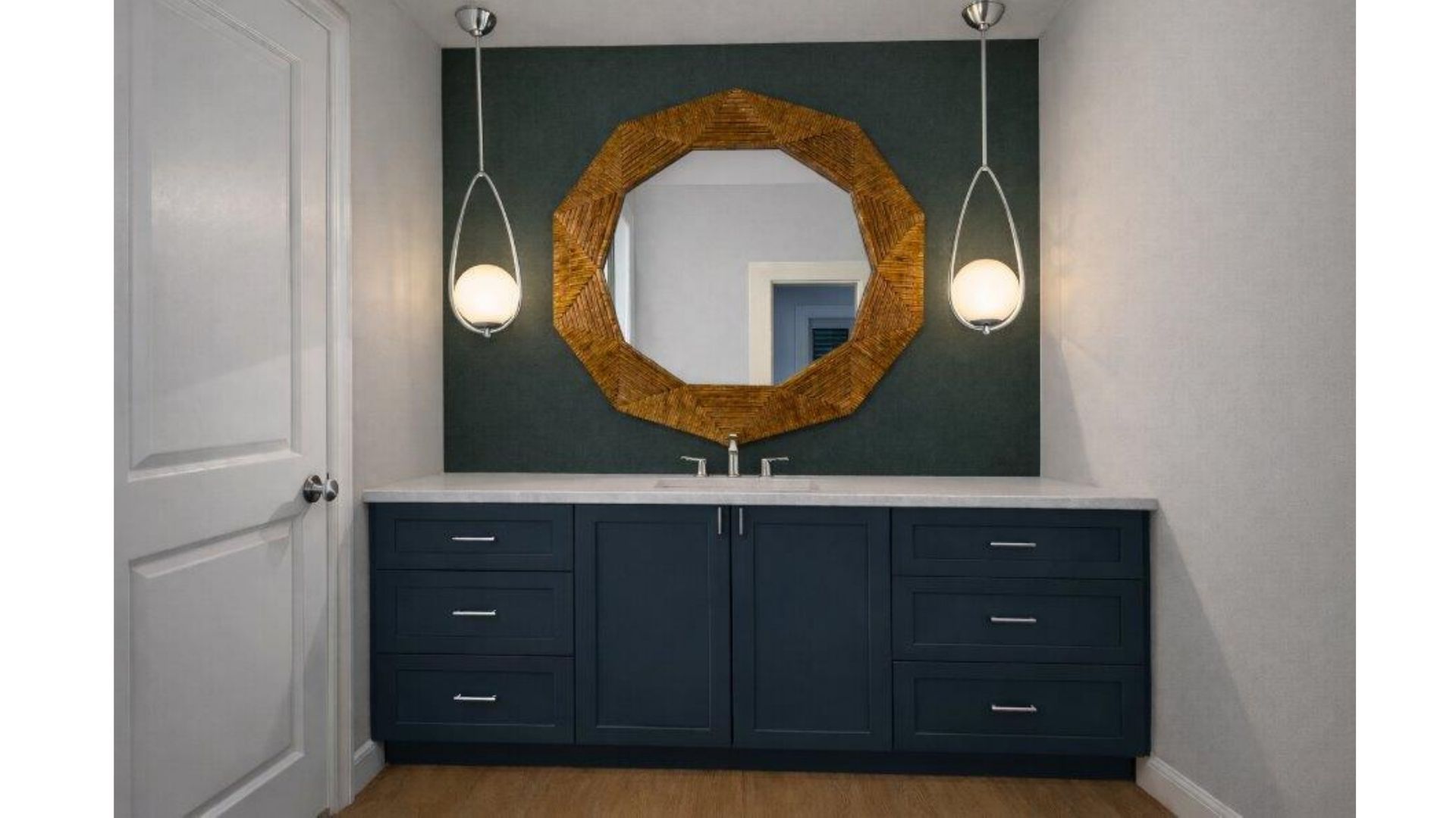Modern entryway with navy console, round gold mirror, and two hanging pendant lights on a dark accent wall.
