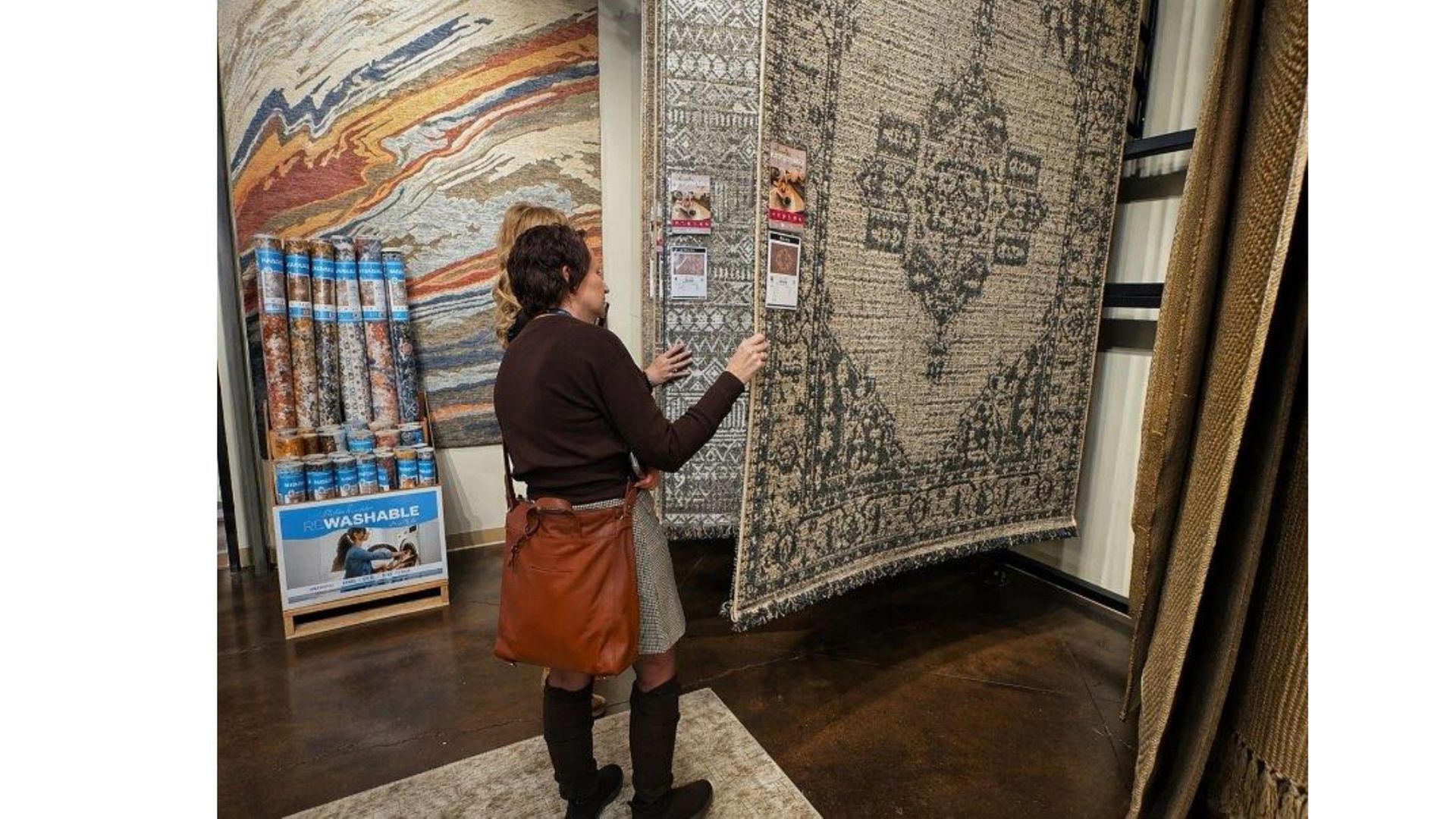 Person photographing a large wall tapestry in a museum-like gallery with patterned artworks and dark wood flooring