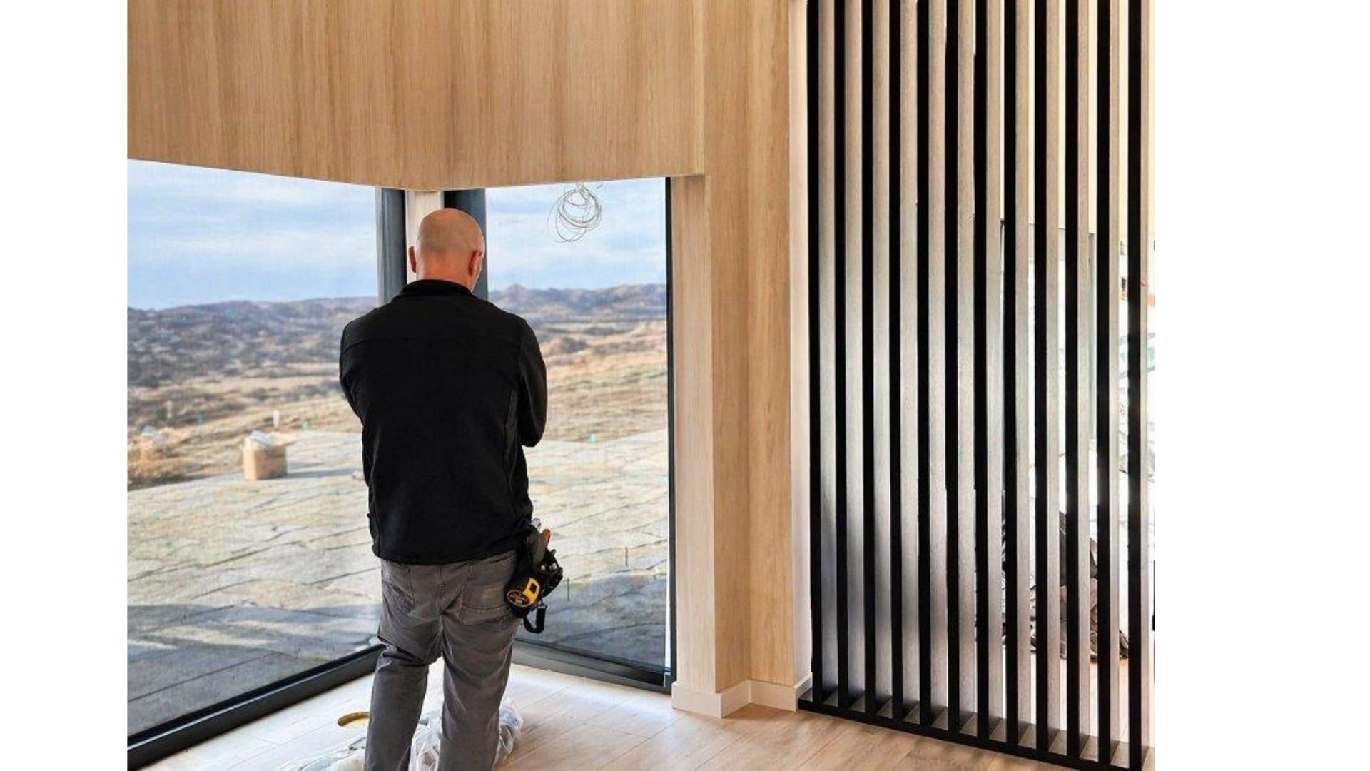 Person standing by a large floor-to-ceiling window, looking out at a desert landscape from a modern interior