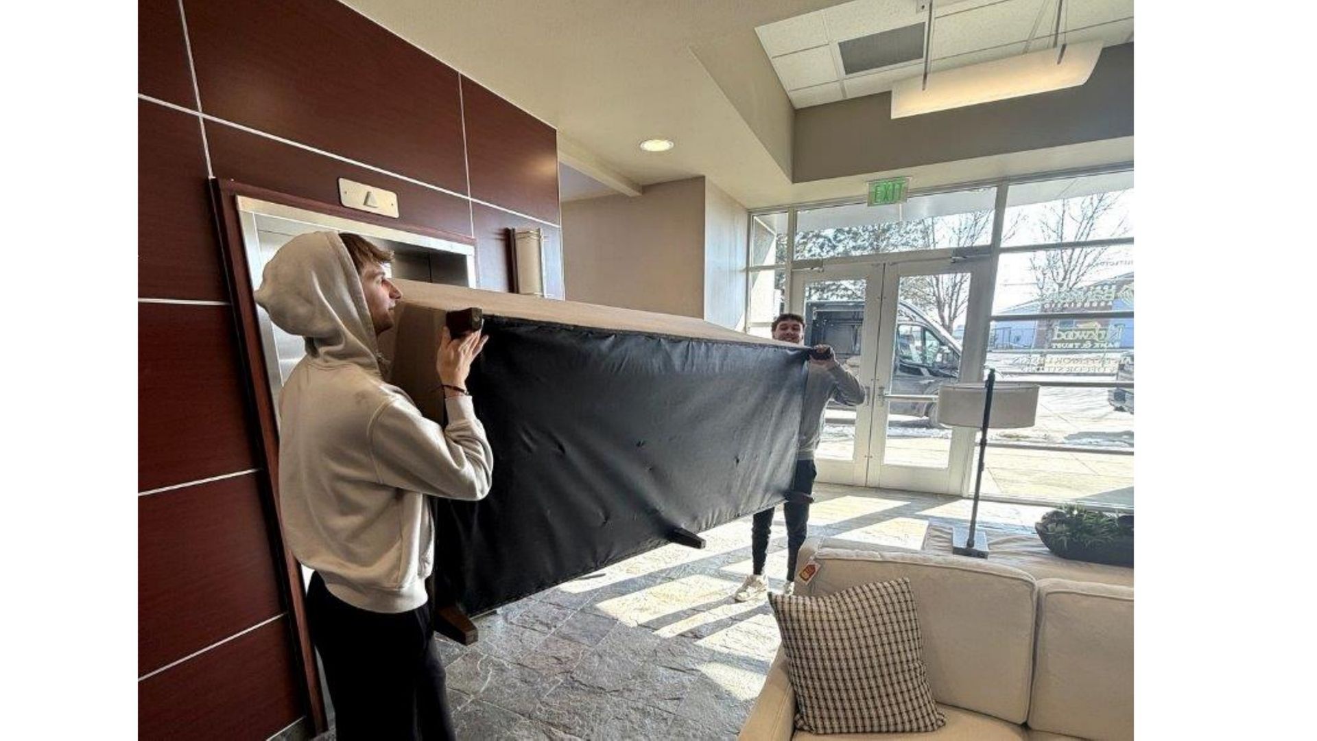 Person hanging a large black curtain in a bright lobby near glass doors