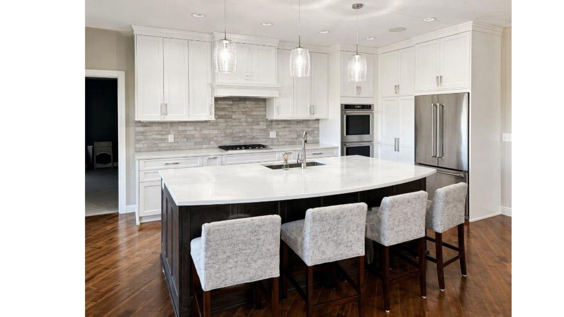 Modern white kitchen with marble island, four gray stools, stainless steel refrigerator, and dark wood floor