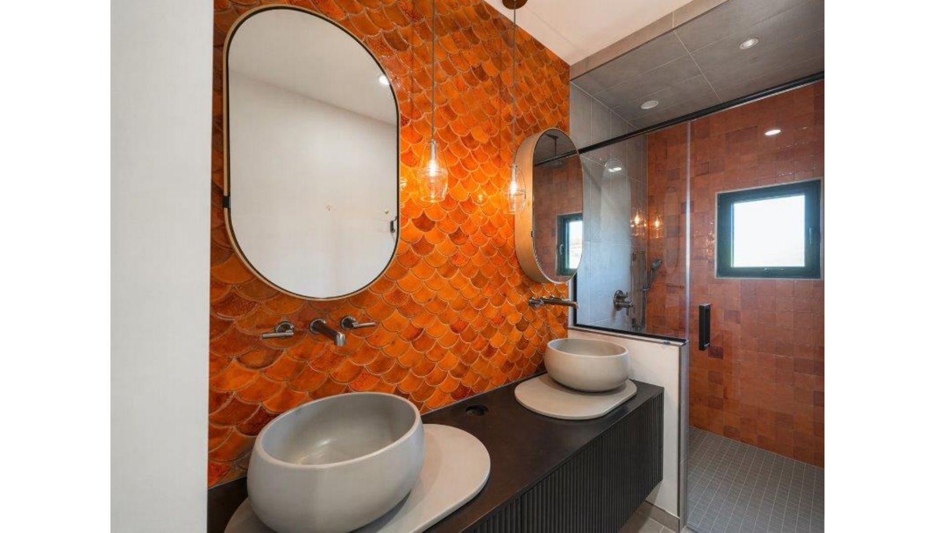 Modern bathroom with orange mosaic walls, two vessel sinks, and a large oval mirror