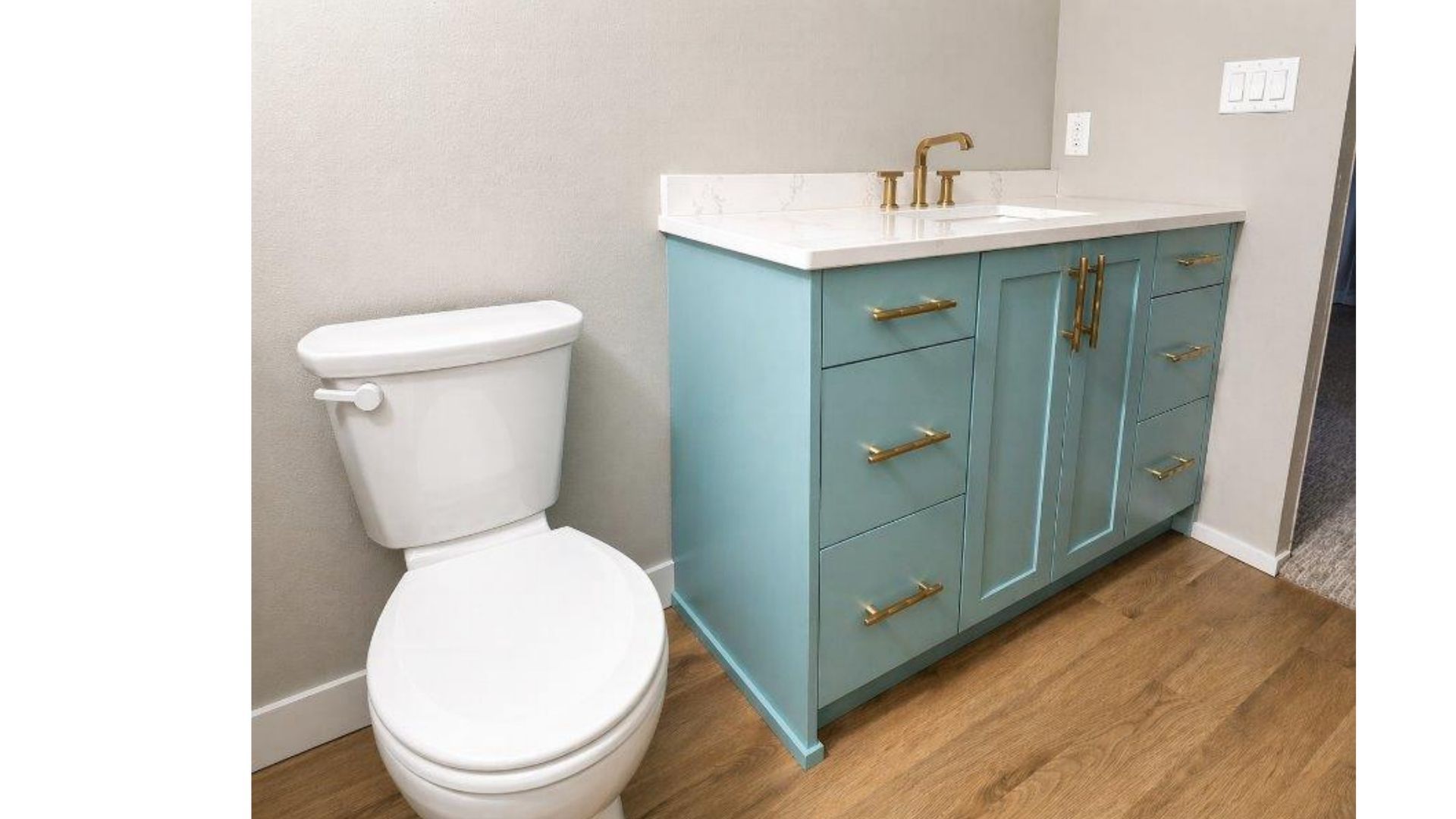 Small bathroom with a white toilet and blue vanity with gold handles and sink.
