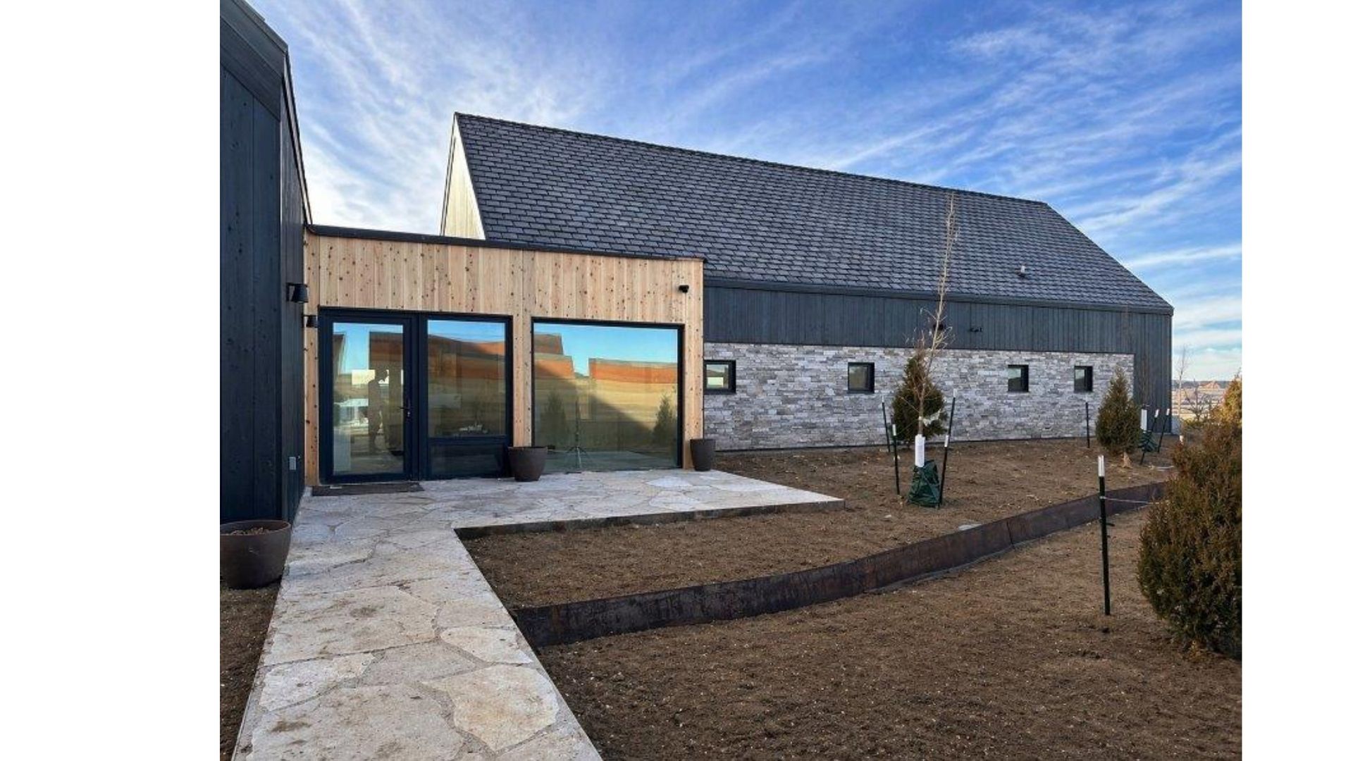 Stone building entrance with glass doors, slate roof, and a stone walkway under a blue sky.