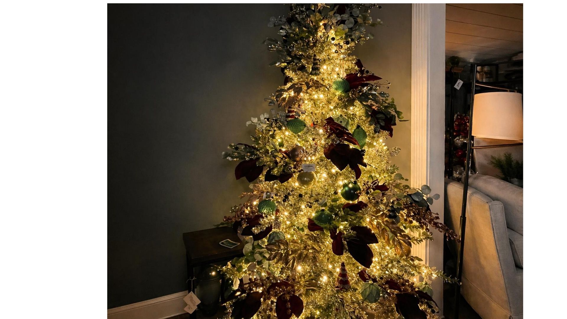 Lit Christmas tree with gold lights and dark ornaments beside a doorway in a dim room