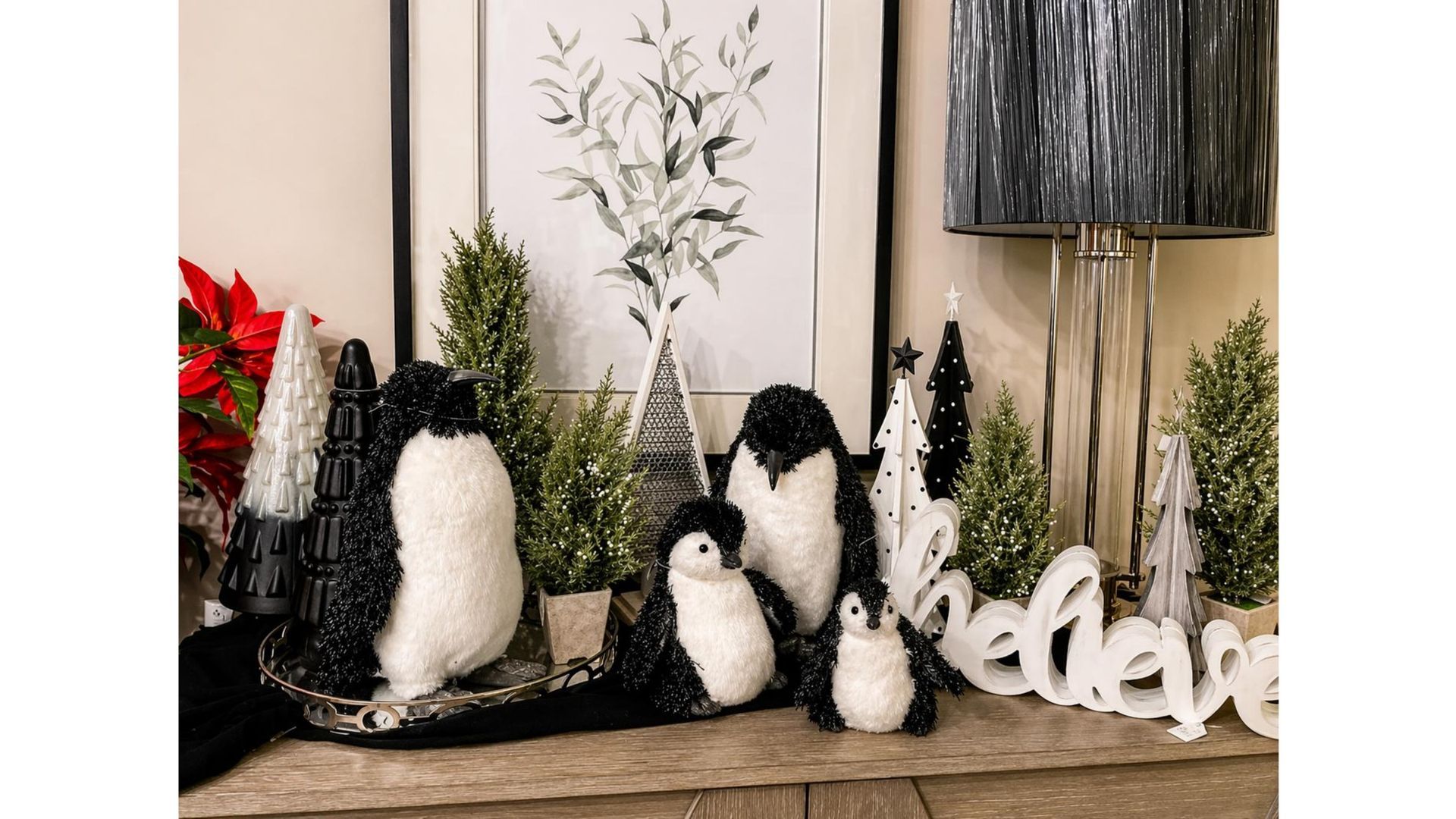 Decorative black-and-white penguin figurines on a mantel with pine trees and a “believe” sign