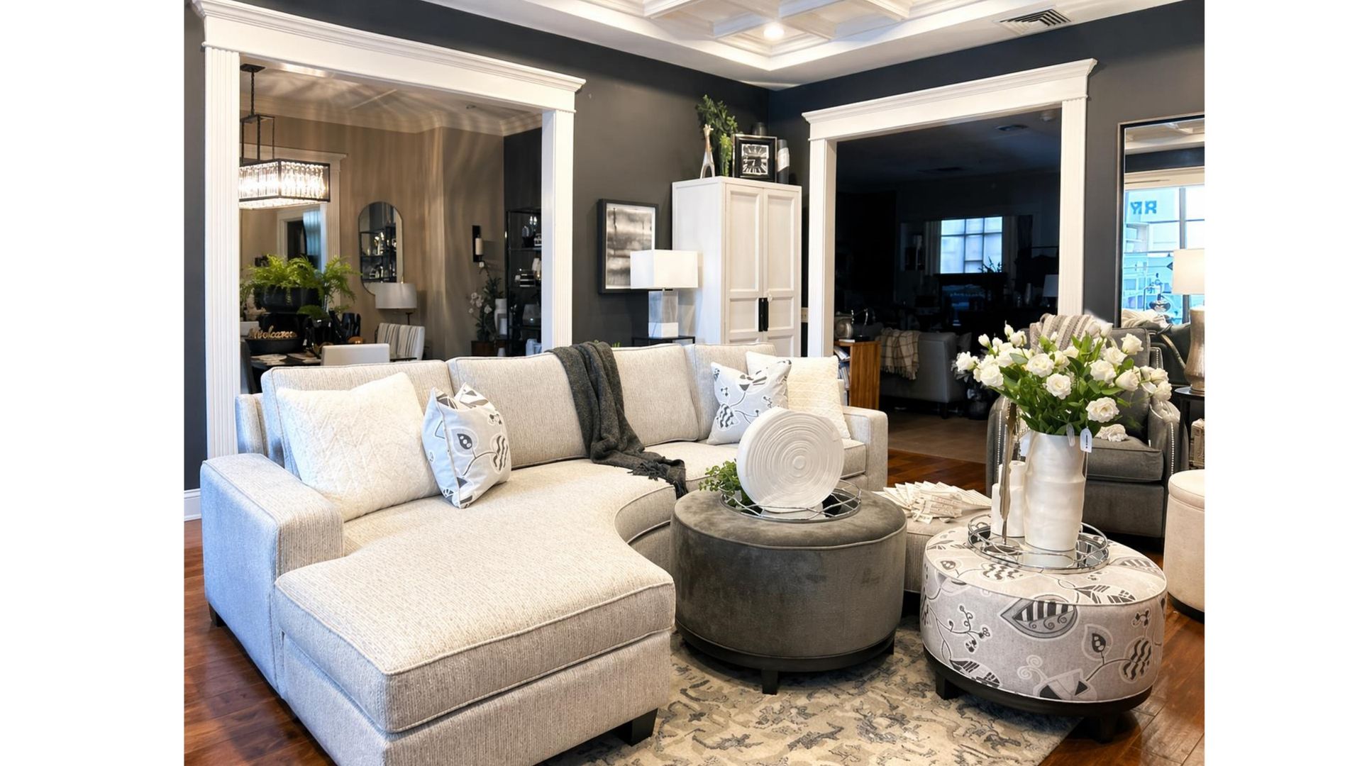 Bright living room with cream sofa, round ottomans, mirrored wall, and floral arrangement