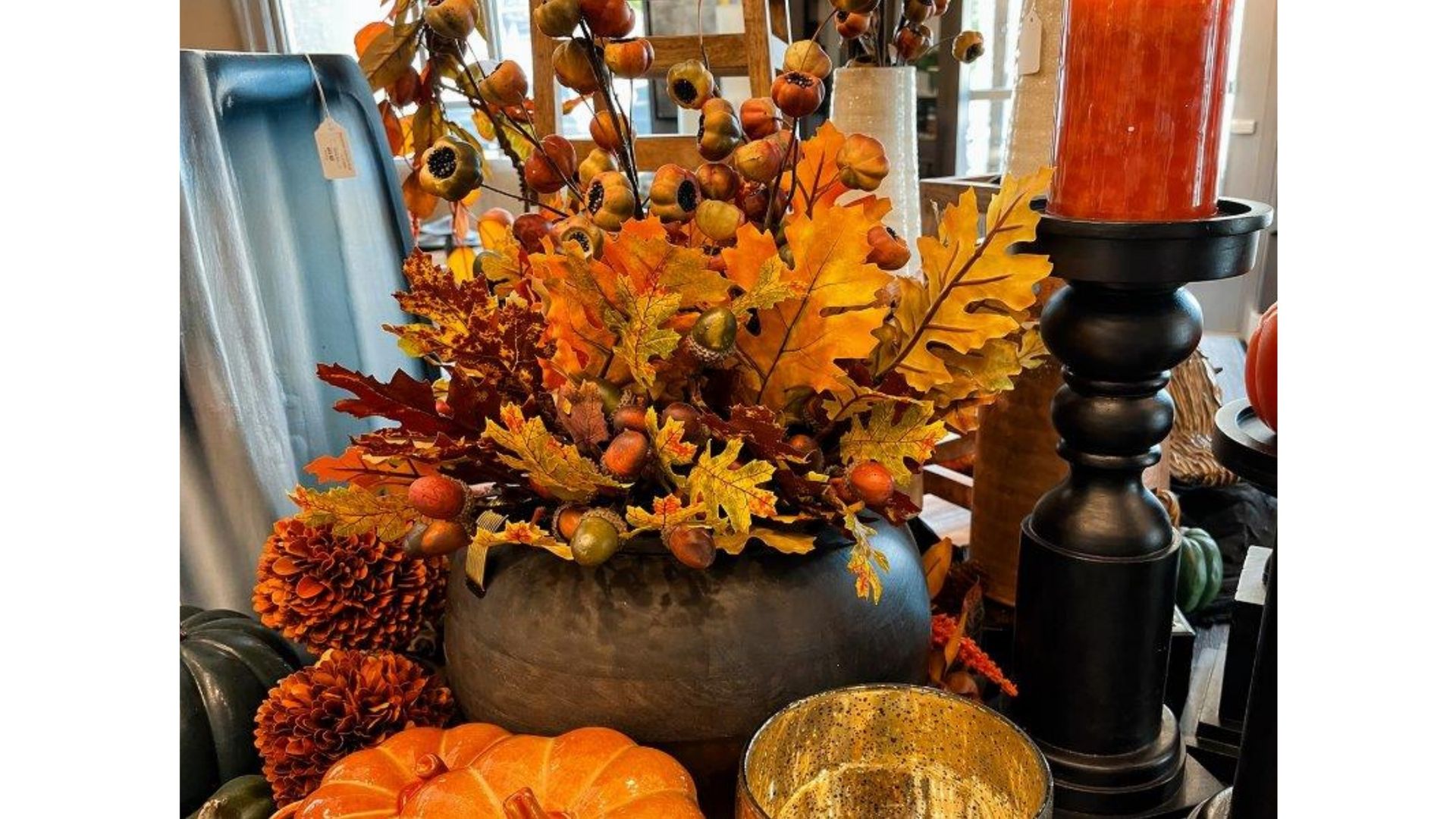 Autumn floral arrangement with orange leaves, pumpkins, and candles on a rustic table