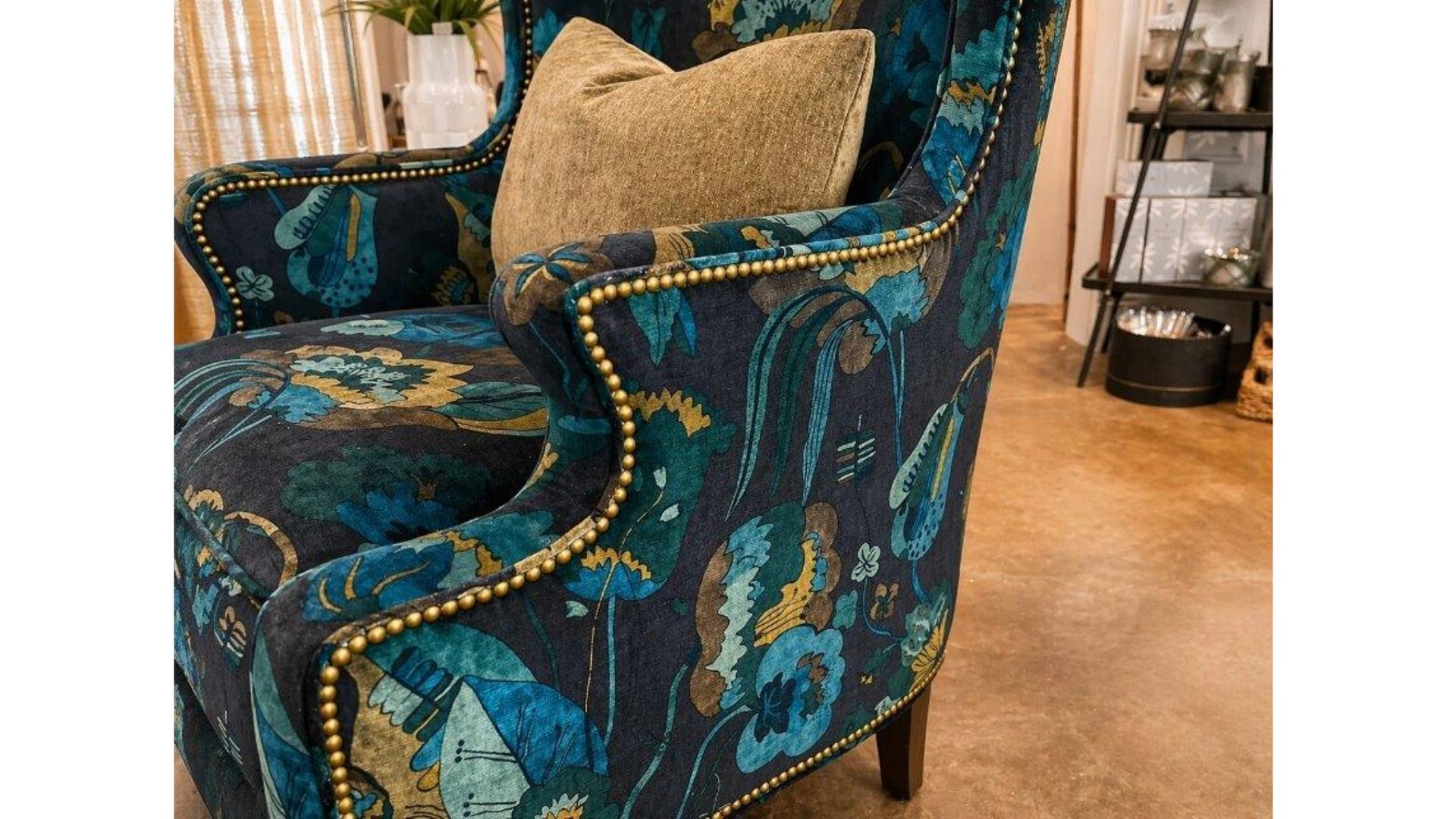 Teal patterned armchair with gold trim and beige pillow on a wood floor indoors