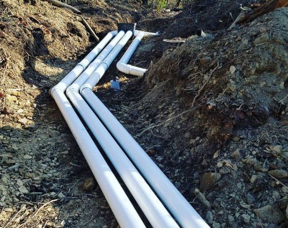 A bunch of white pipes are laying in the dirt