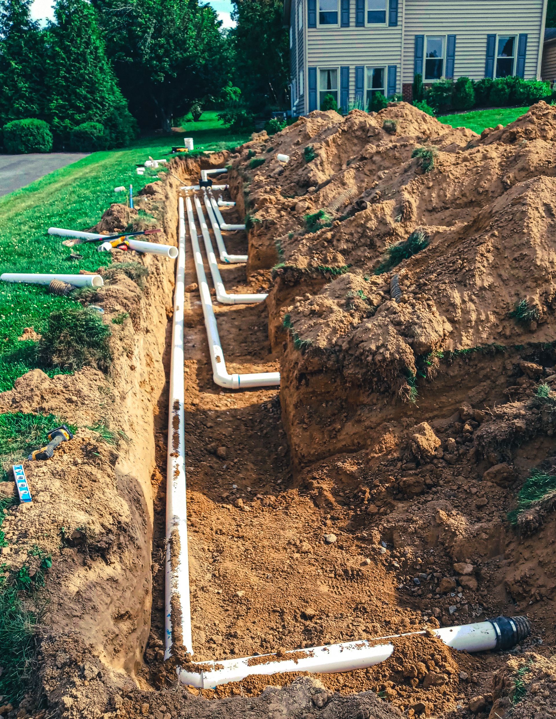 A row of pipes are being installed in the dirt in front of a house.