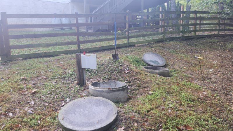 There are two septic tanks in the grass next to a wooden fence.