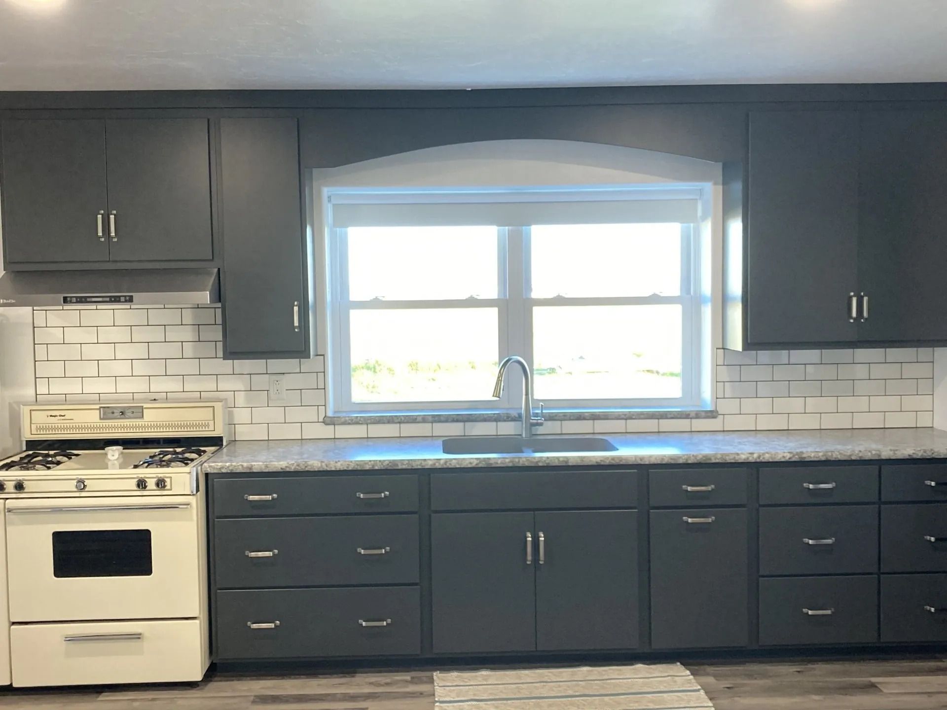 Kitchen with dark gray cabinets, white subway tile backsplash, and a window above the sink.