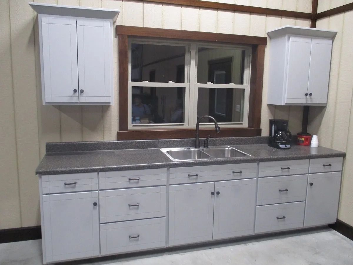 Kitchen with light gray cabinets, dark countertop, double sink, window, and small appliances.