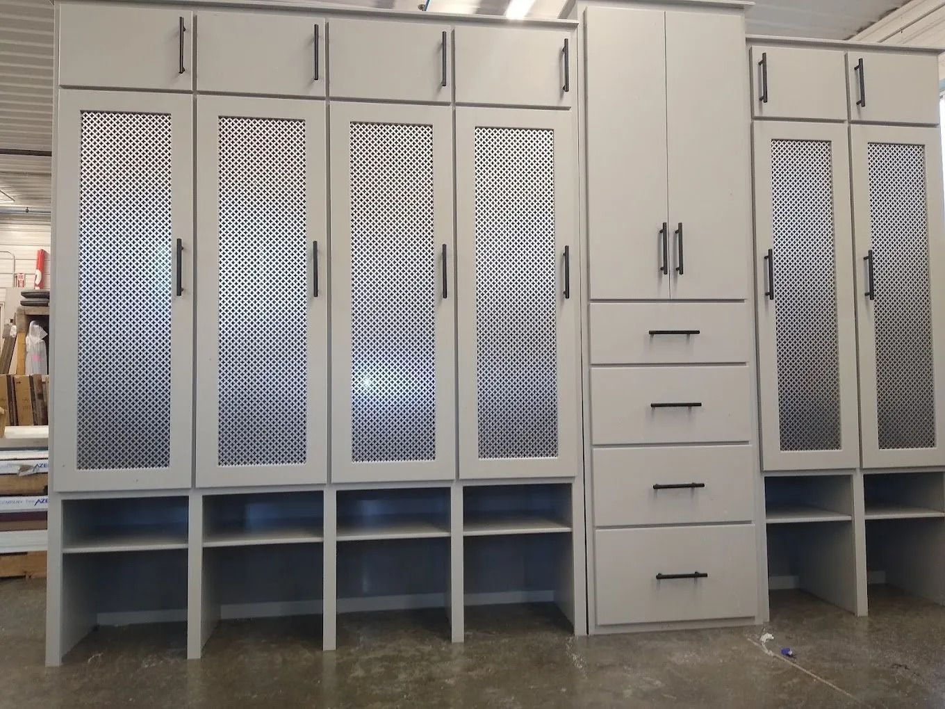 Light gray custom cabinets with patterned glass doors and lower open shelves in a workshop.