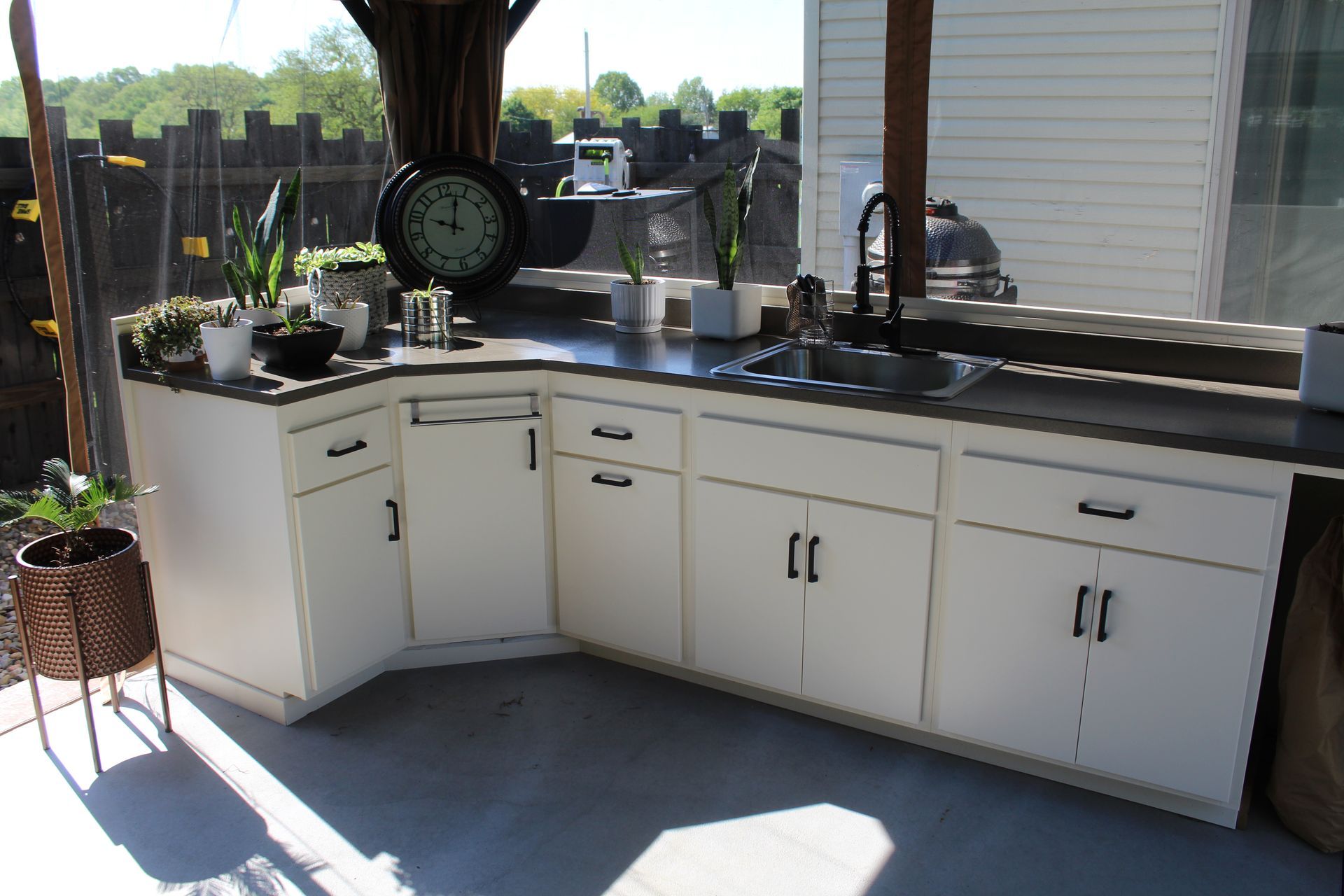 Outdoor kitchen with white cabinets, concrete countertop, and a large clock.