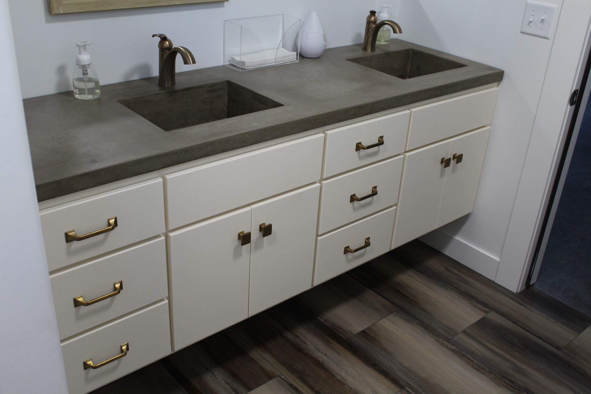 Bathroom vanity with two sinks, gray countertop, white cabinets, and gold hardware.