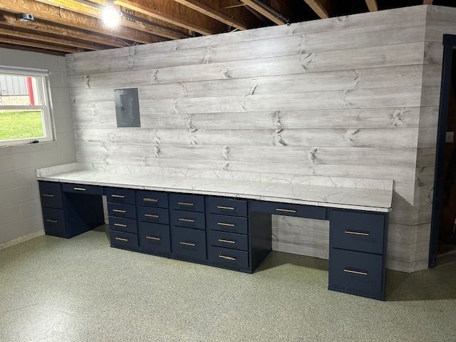 Workshop with long blue cabinets, white countertop, and weathered wood wall. Gray flooring.