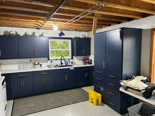 Navy kitchen with white countertops and cabinets against exposed beams.