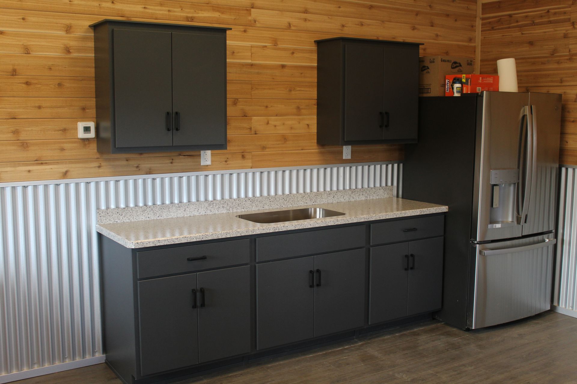 Garage kitchen with gray cabinets, stainless steel refrigerator, and corrugated metal wainscoting.
