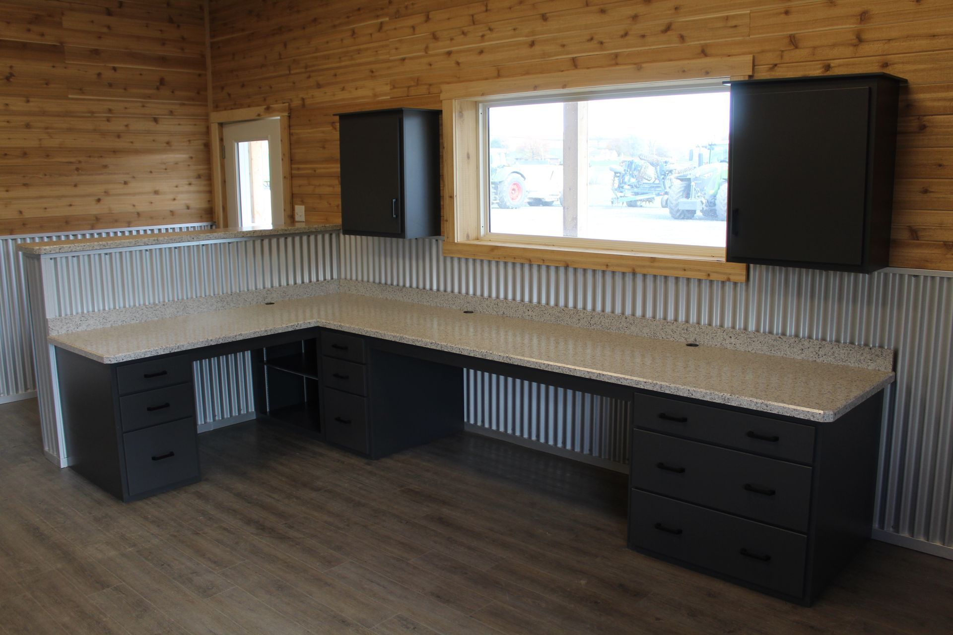 L-shaped office desk with dark cabinets, tan countertop, and corrugated metal wall.