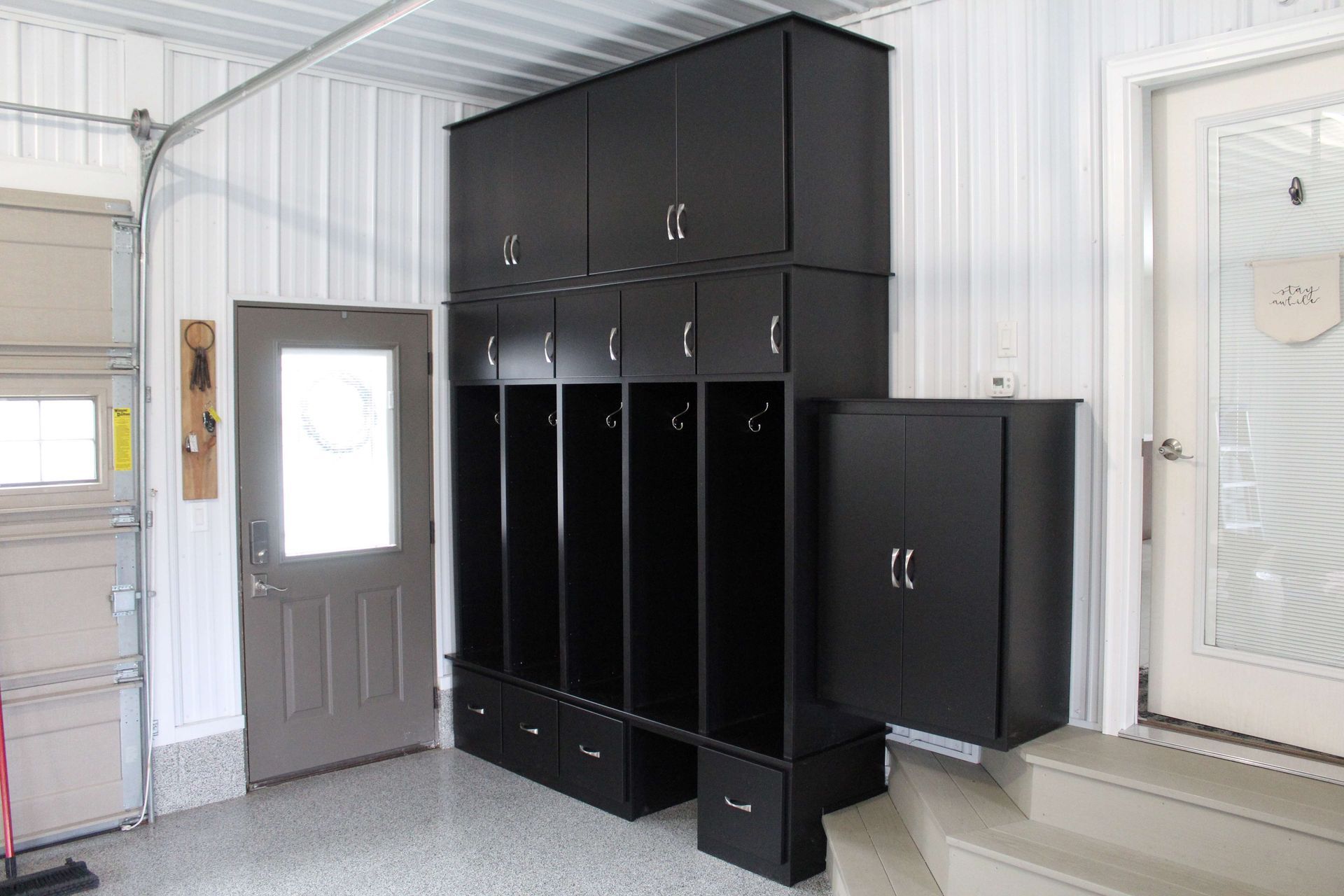 Black storage cabinets in a garage. Includes lockers, drawers, and cabinet doors. A door is on either side.