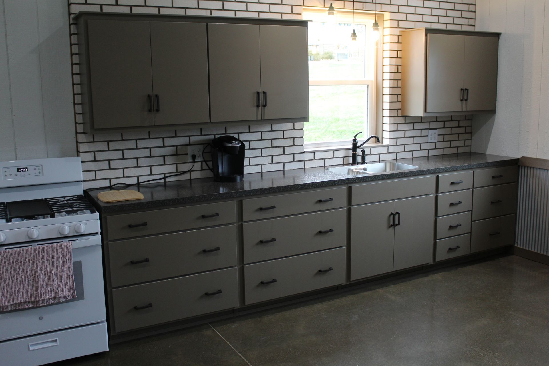 Kitchen with gray cabinets, black countertops, and a white brick backsplash.